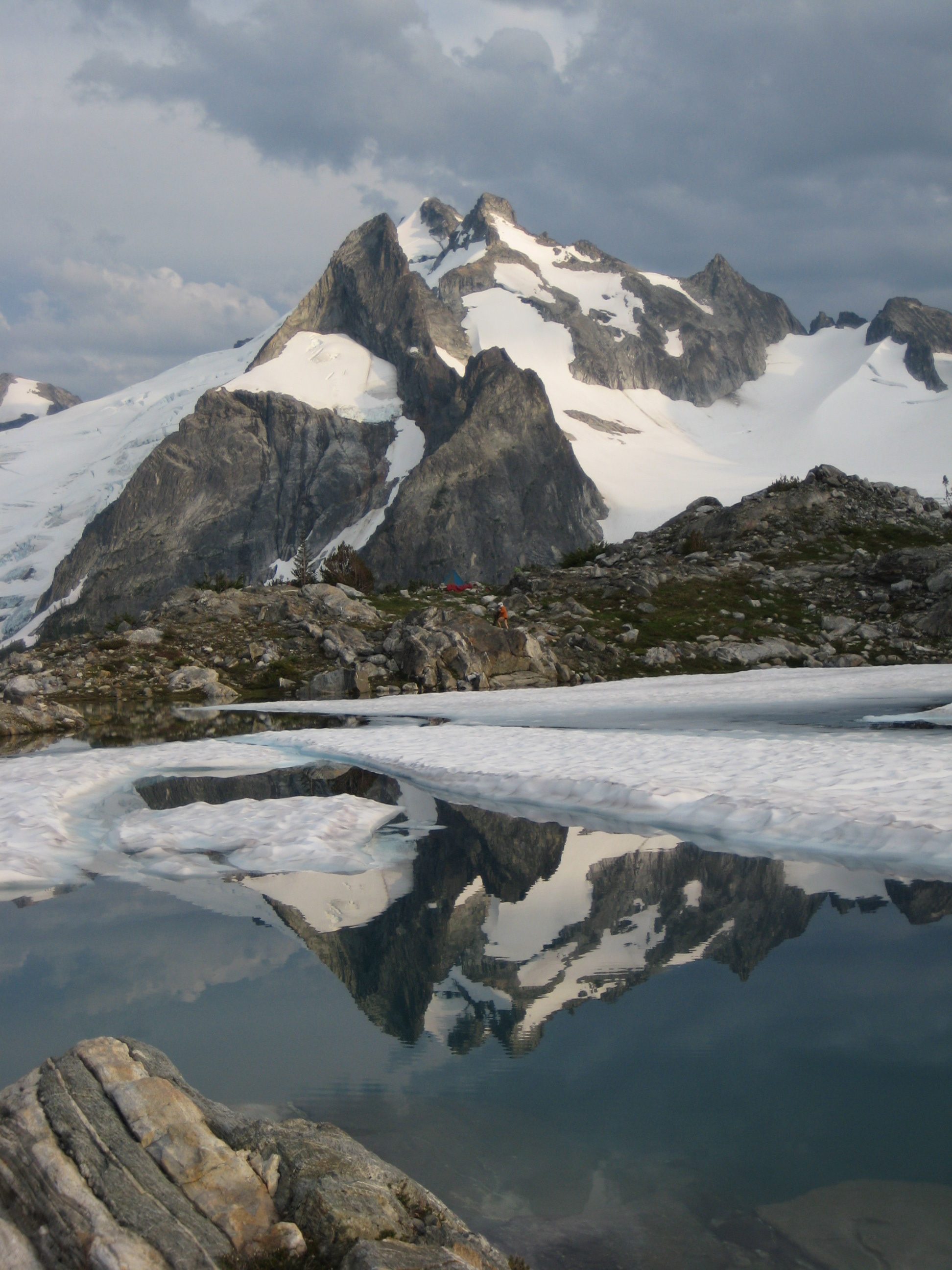 Dome Peak reflecting in White Rock Lakes with floating snow patches along the Ptarmigan Traverse
