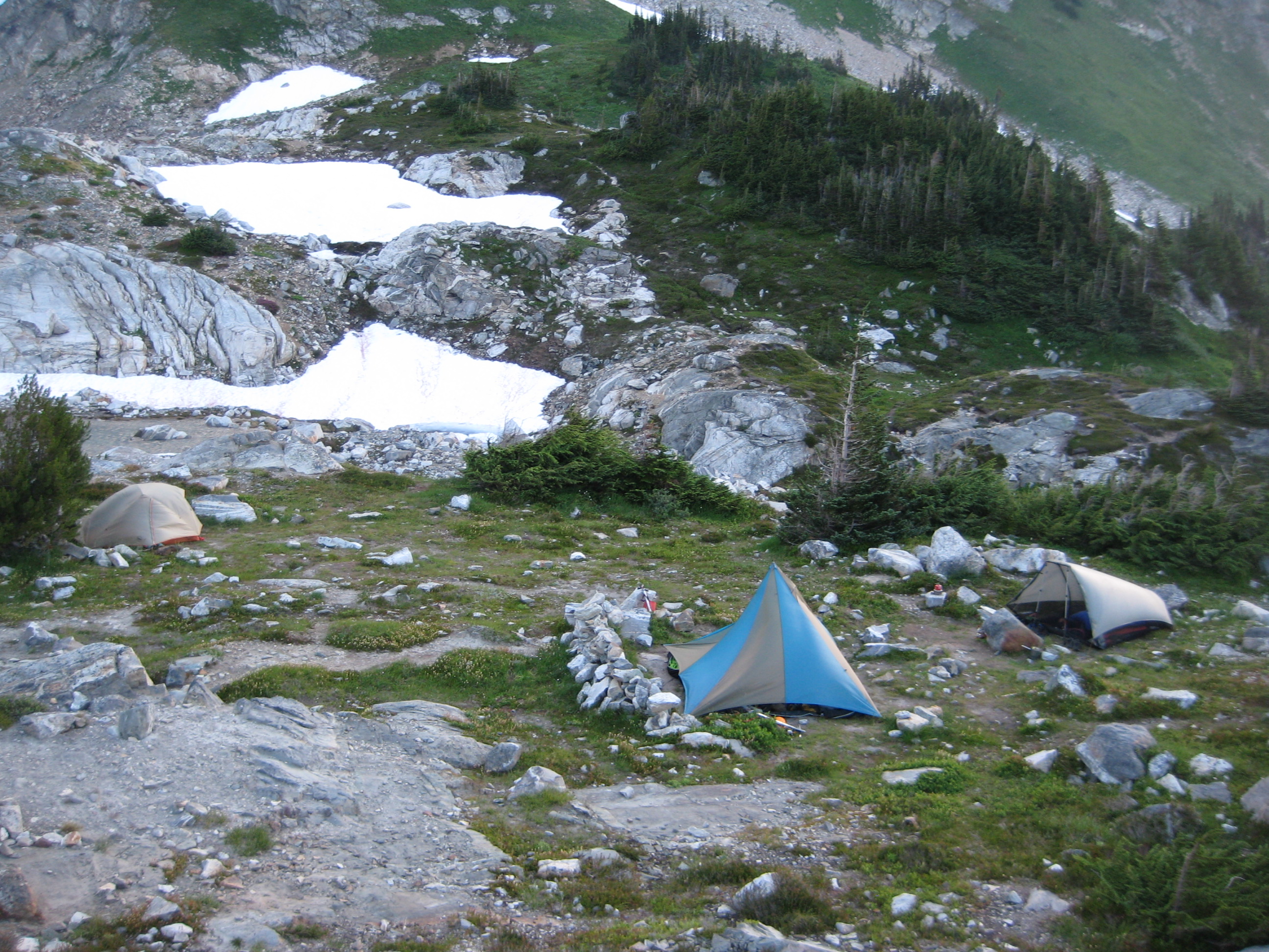 mountain climber's camp on the rocky shores of White Rock Lakes along the Ptarmigan Traverse with linguring snow patches