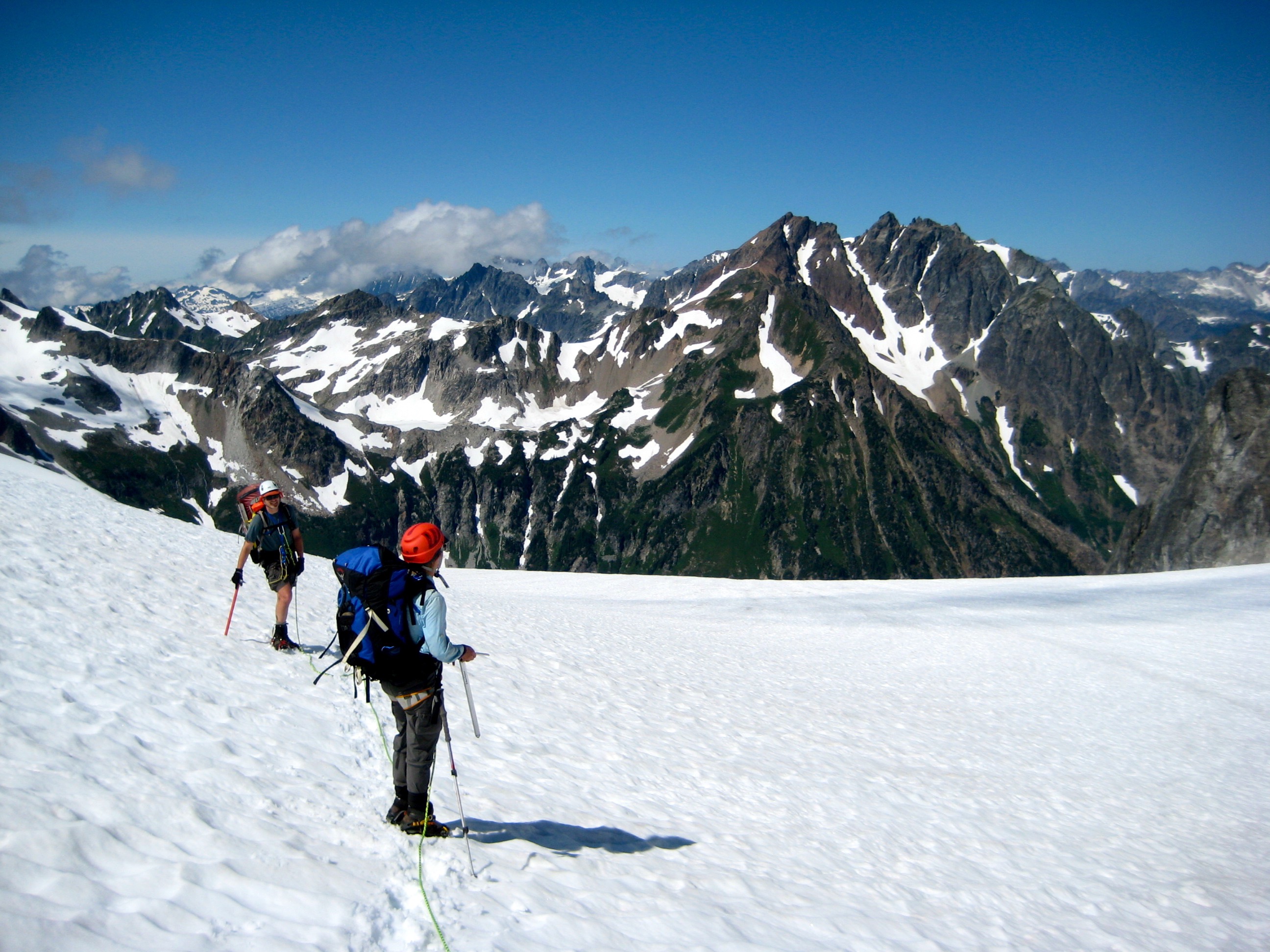 roped mountain climbers taking a break on snow field along the Ptarmigan Traverse with Sentinal and Old Guard Peask in the background