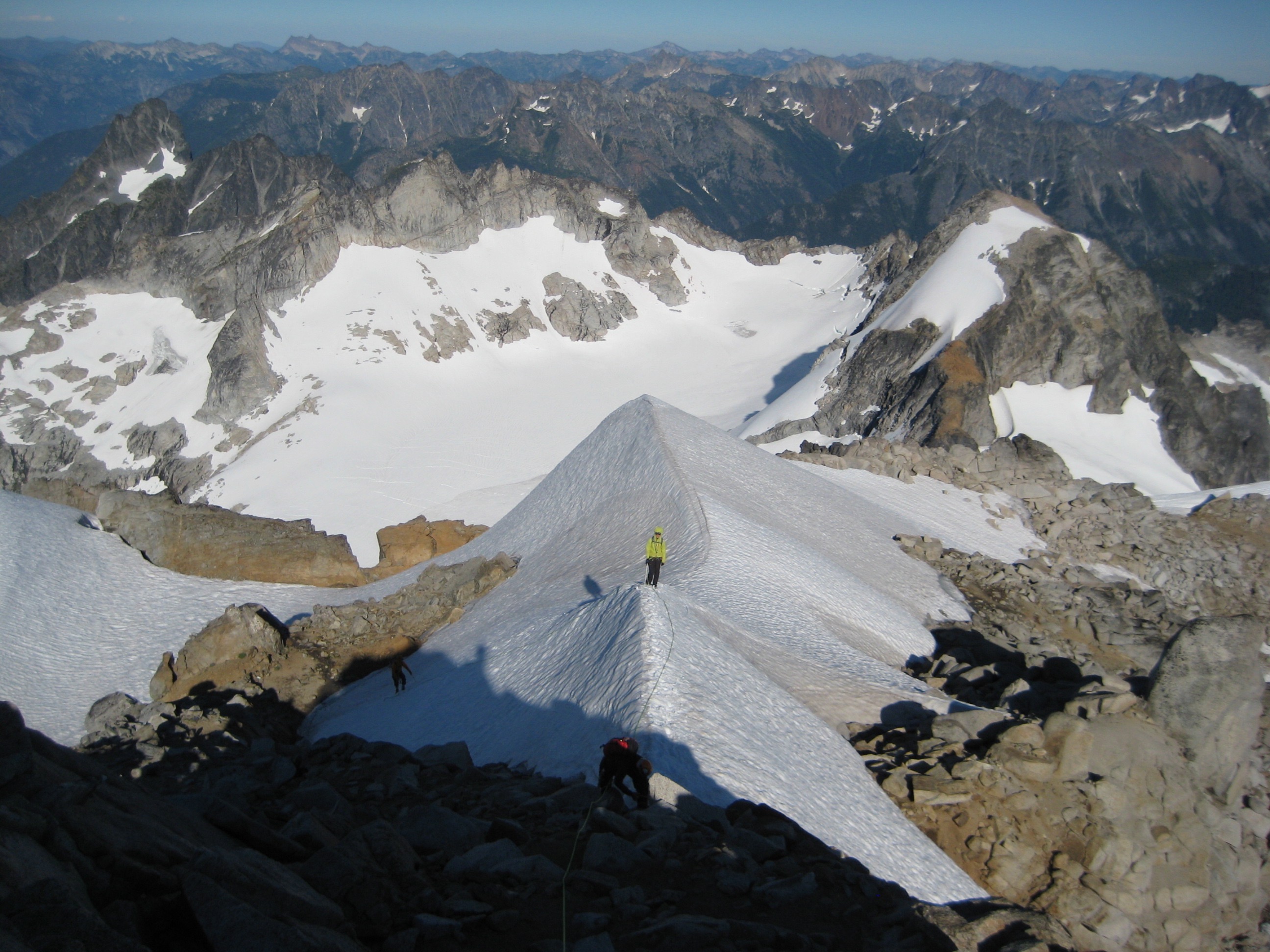 mountain climber on the snowy ridge of Dome Peak with the Ptarmigan Mountains in the background