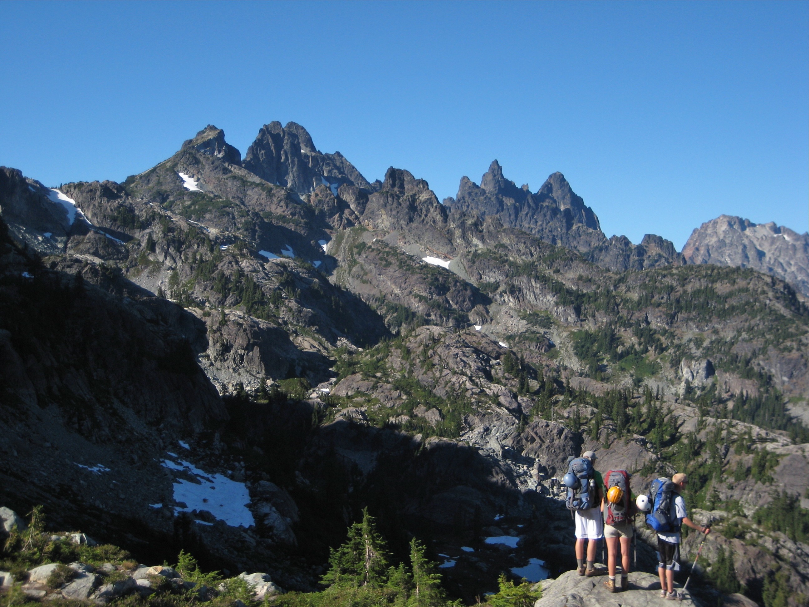 Lemah Mountain and Chimney Rock in the Alpine Lakes Wilderness with three climbers standing on a rocky edge enjoying the view