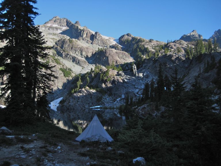 A camping tent is pitched below the rocky summit of Chikamin Peak in the Alpine Lakes WIlderness