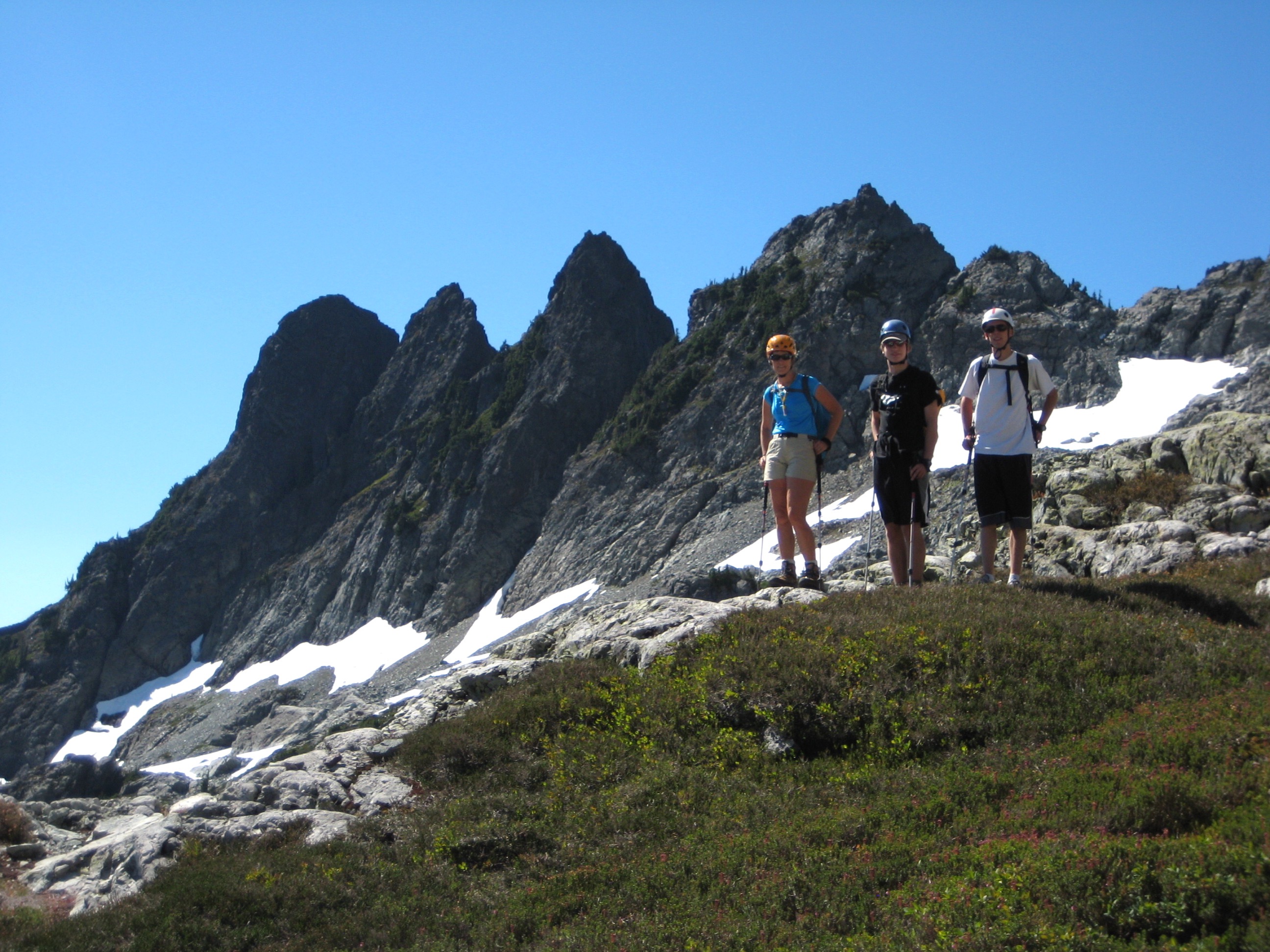 three climbers standing in the heather with Four Brothers Mountain in the background