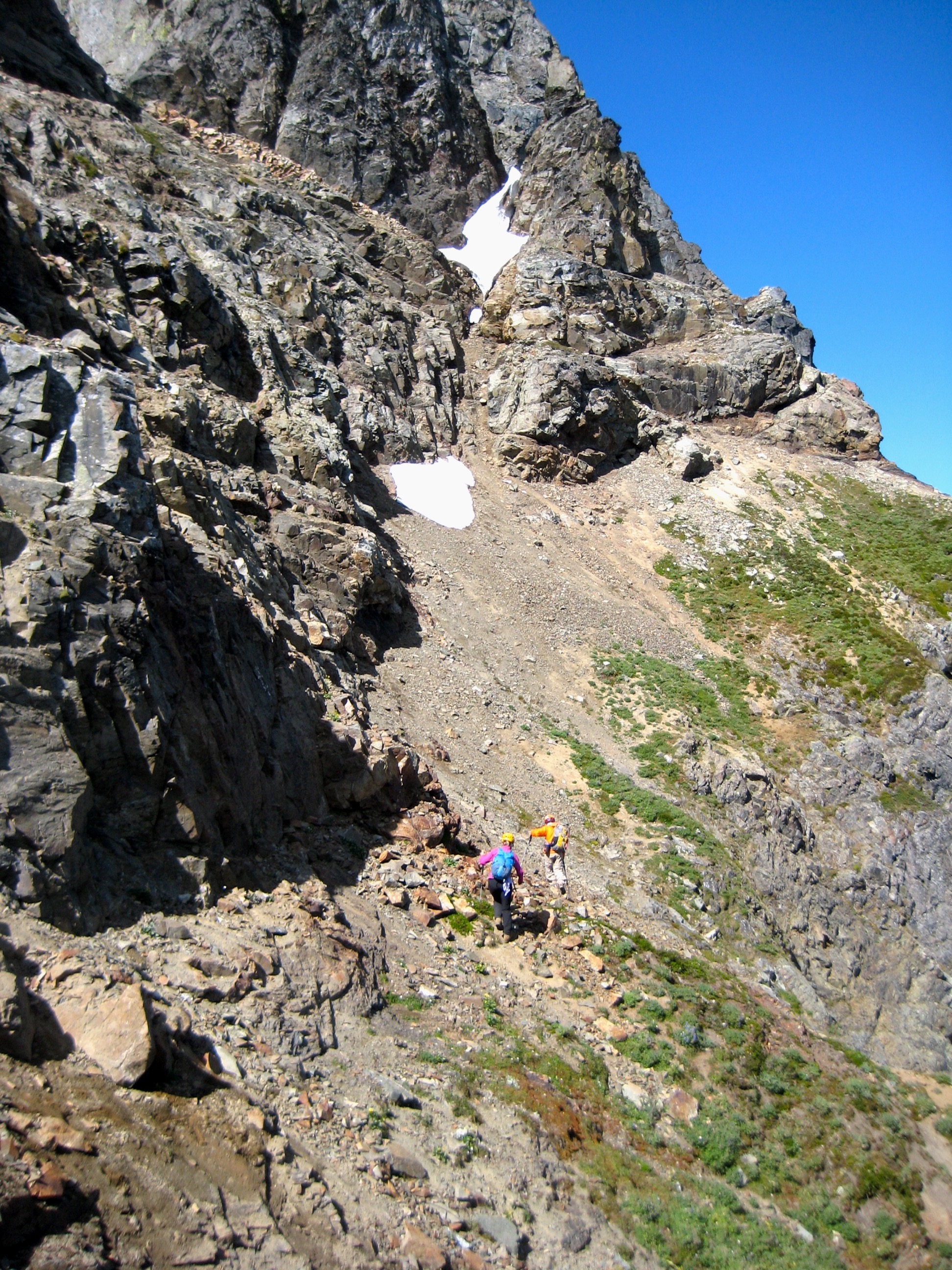 mountain climbers traversing steep scree under rocky cliffs of American Border Peak in the Mt Baker Wilderness