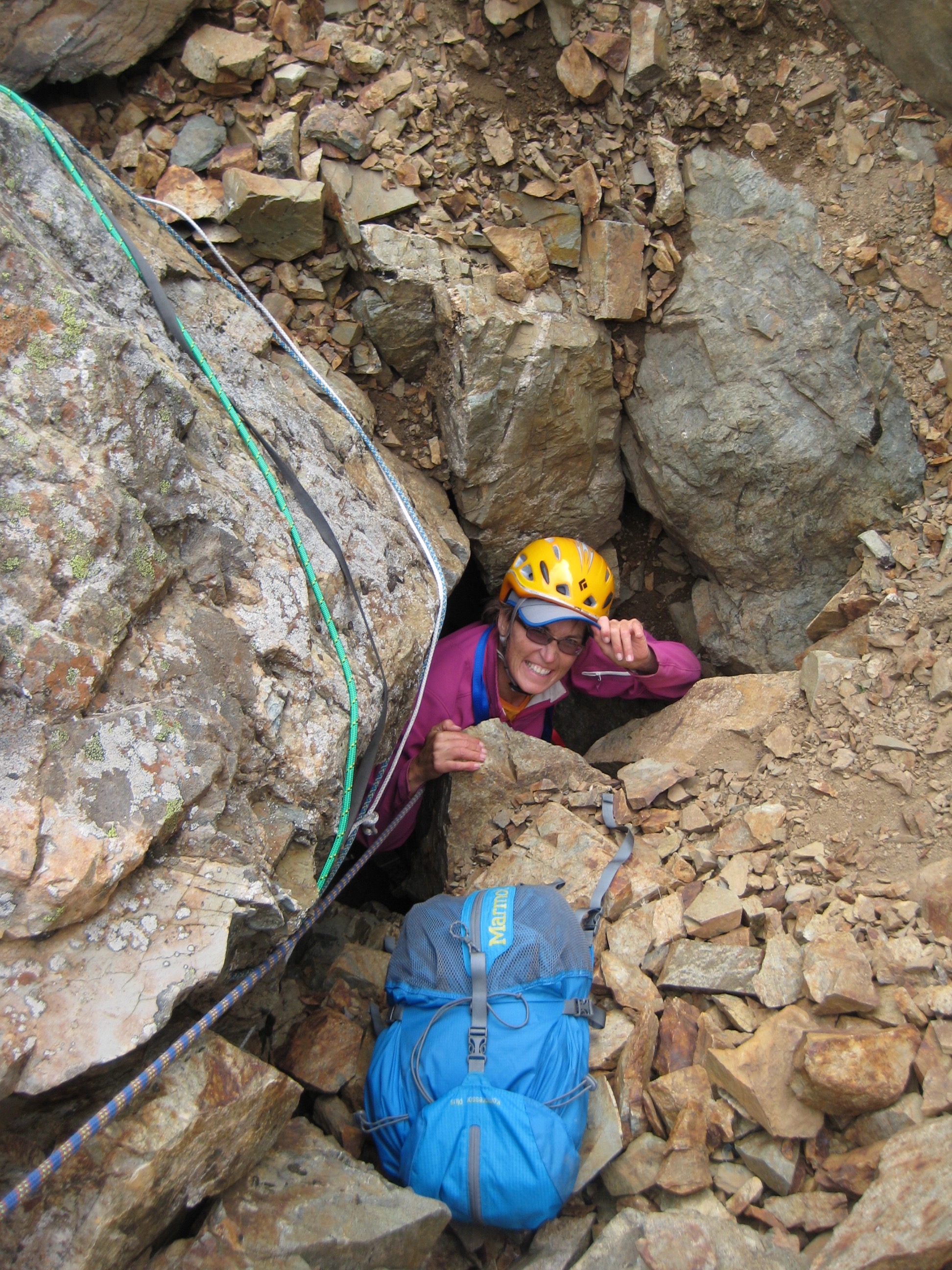 mountain climber scrambling through cannonhole with rappel slings and a blue summit pack on American Border Peak