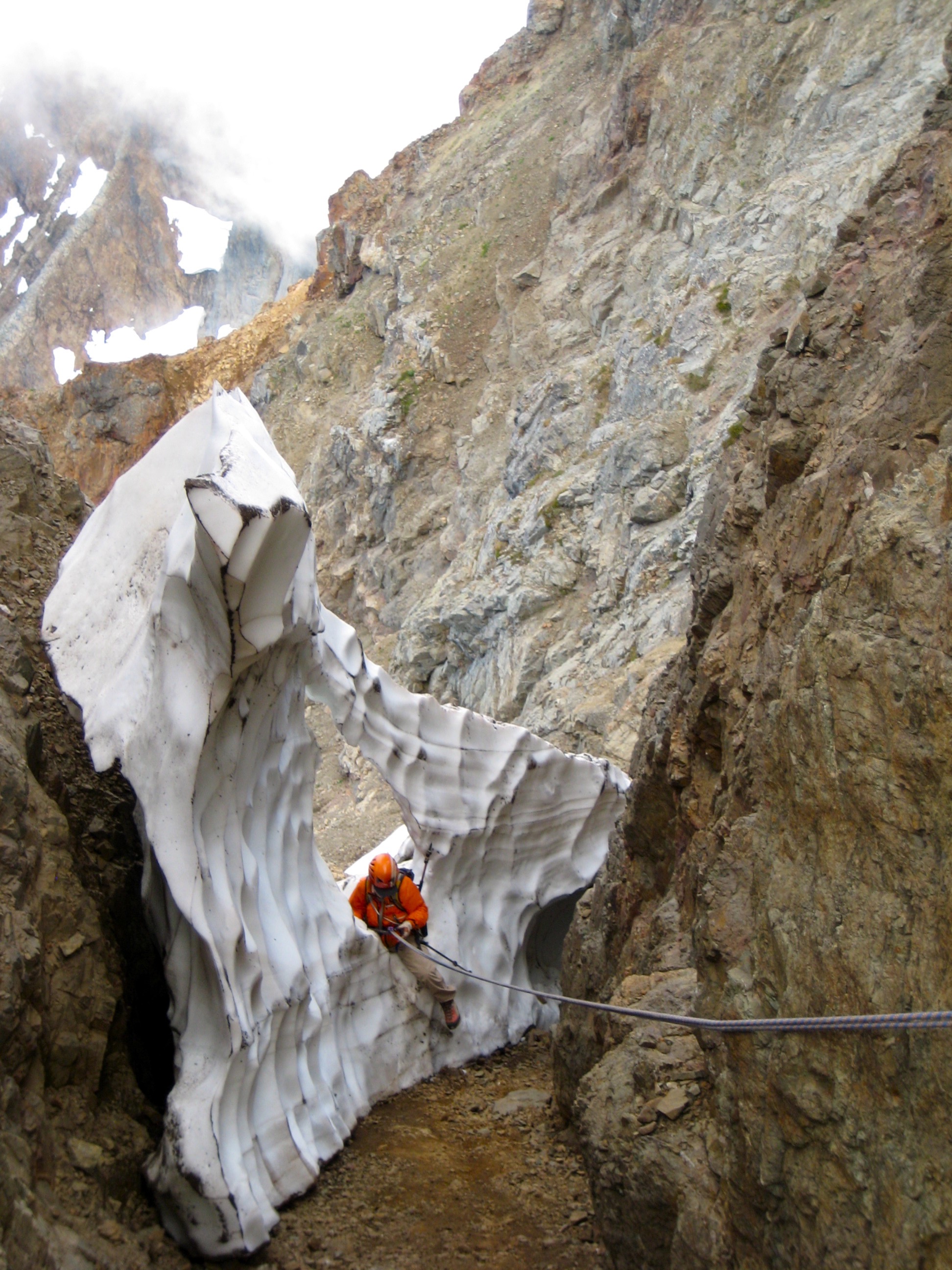 mountain climber rappelling snow cannonhole in the rocky hillside on American Border Peak in the Mt Baker Wilderness