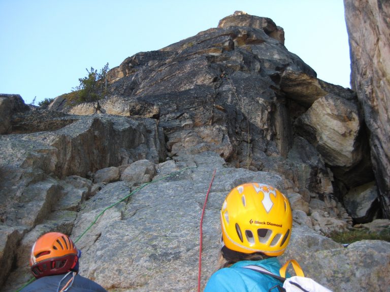Two climbers watch a third climber scale a rock wall on North Early Winters Spire