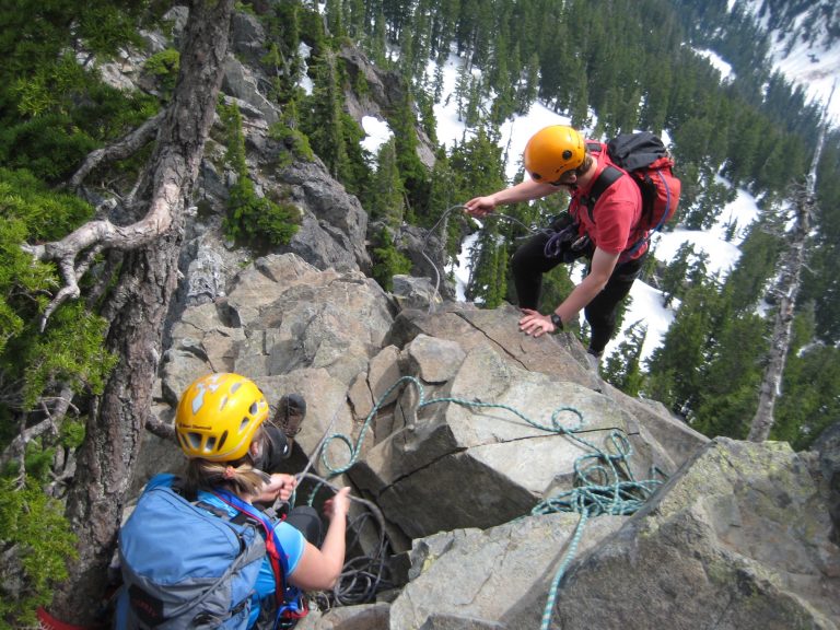 a rock climber belays another climber up a steep face on The Snoqualmie Tooth
