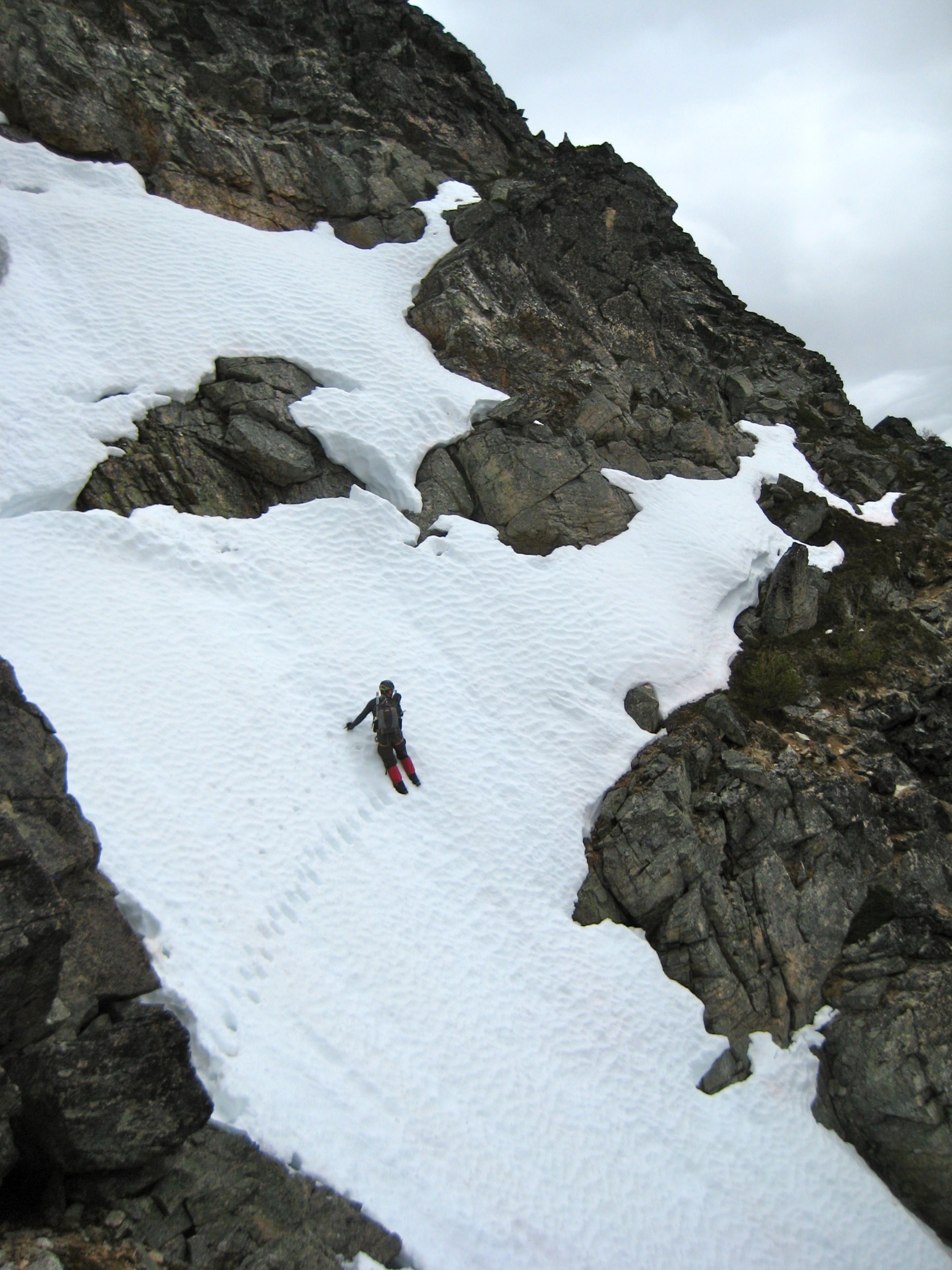 mountain climber facing in traversing a steep snow slope with exposed rock on the shoulder of Kimtah Peak in the North Cascades