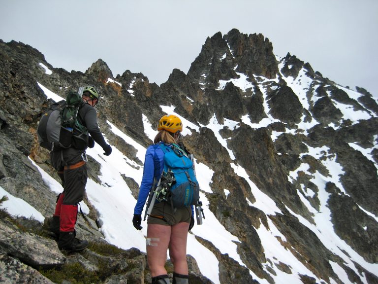 Two mountain climbers stare at a rocky, snowy summit of Kimtah Peak on the Ragged Ridge