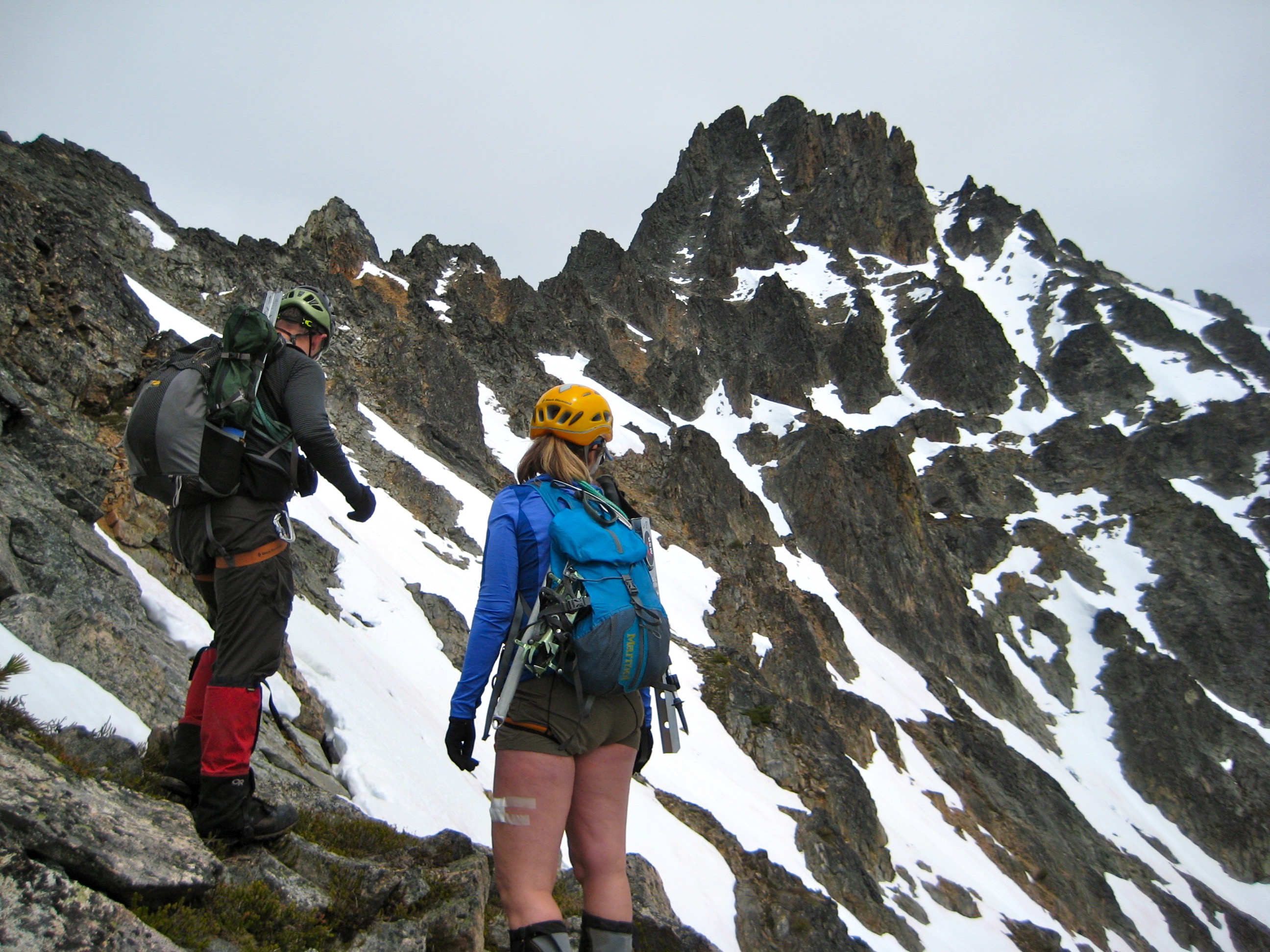 Two mountain climbers stare at a rocky, snowy summit of Kimtah Peak on the Ragged Ridge