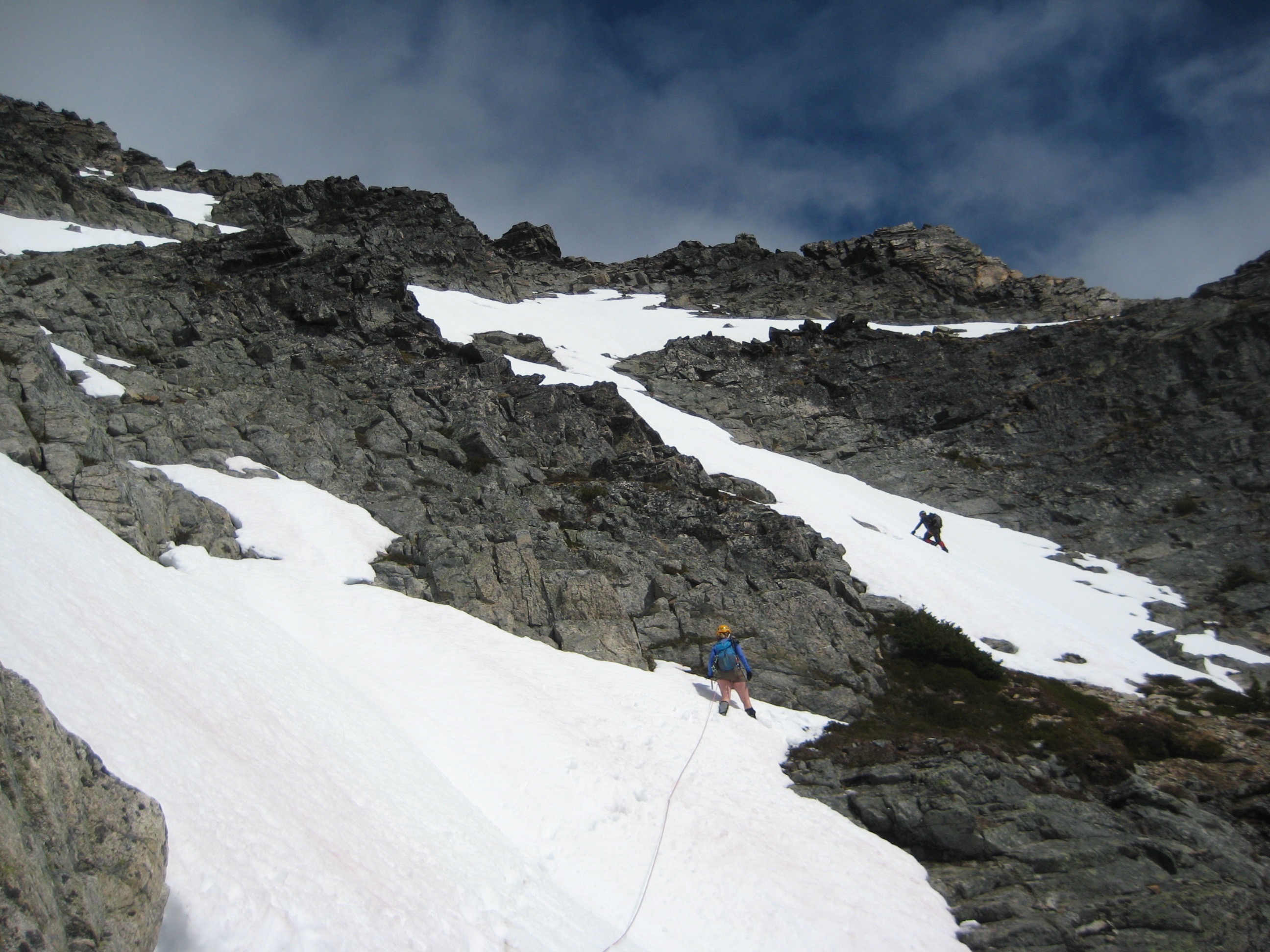mountain climbers ascending snow patches through exposed rock slabs under the summit of Kimtah Peak in the North Cascades