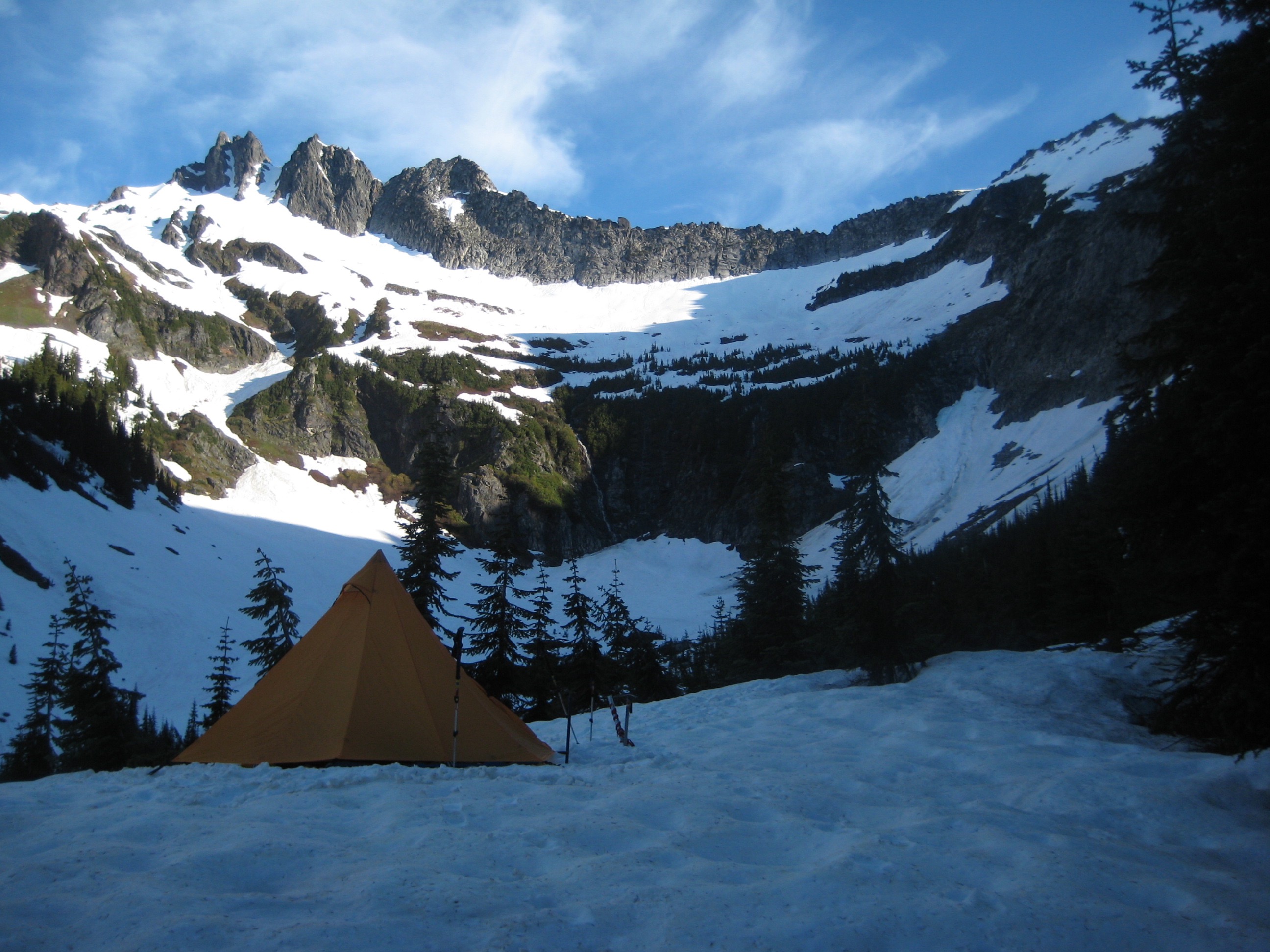 mountain climber's orange tent on snow in Boulder Basin under rocky Clark Mountain in the DaKobed Range in the Glacier Peak Wilderness