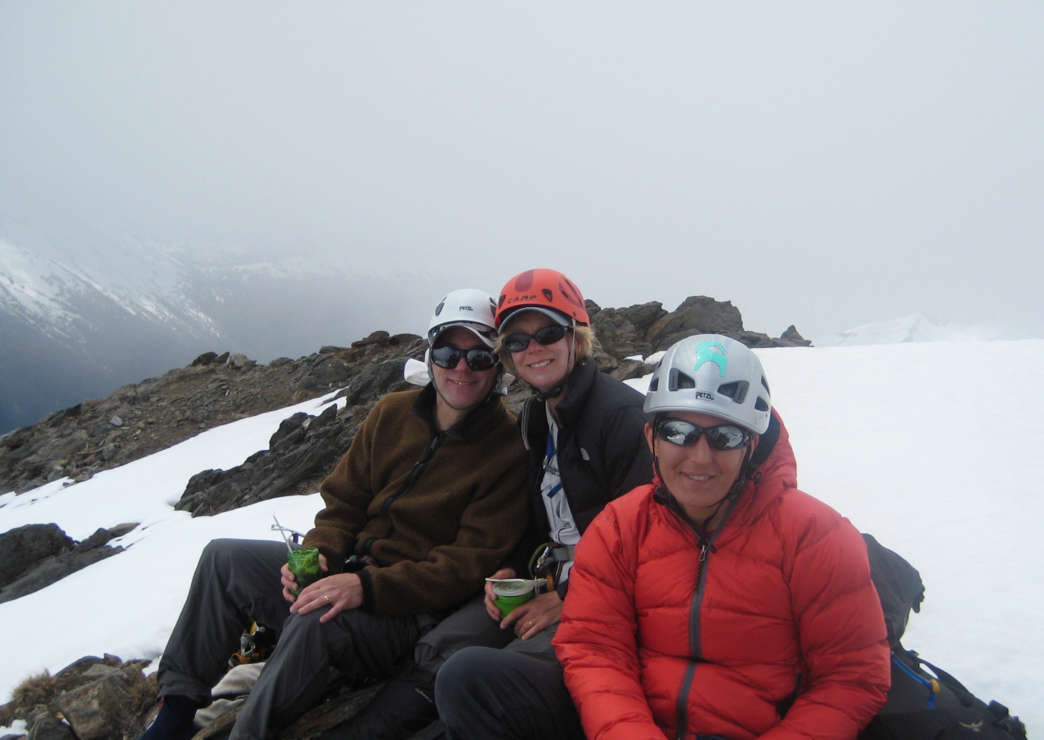 mountain climbers taking a break and smiling on the rock summit of Clark Mountain in the Glacier Peak Wilderness with snow patches