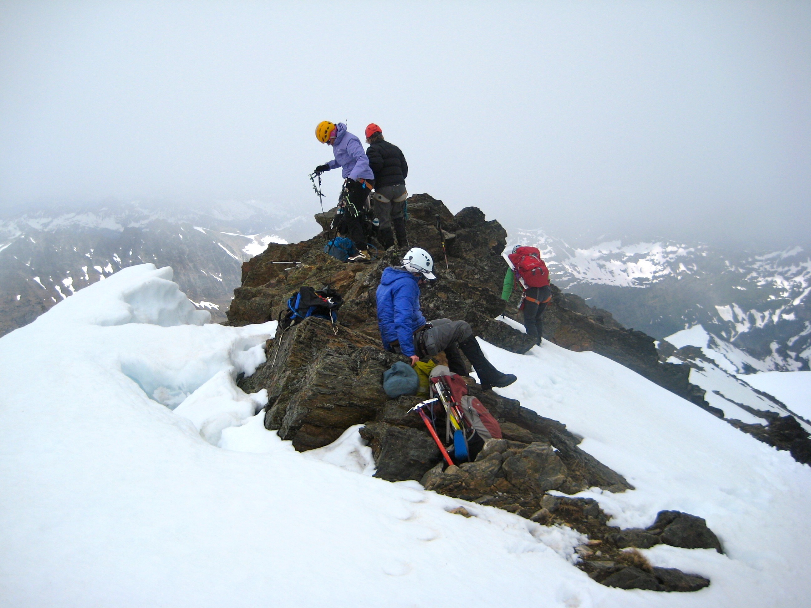 mountain climbers taking a break on the rocky summit of Clark Mountain in the DaKobed Range with snow fields all around 