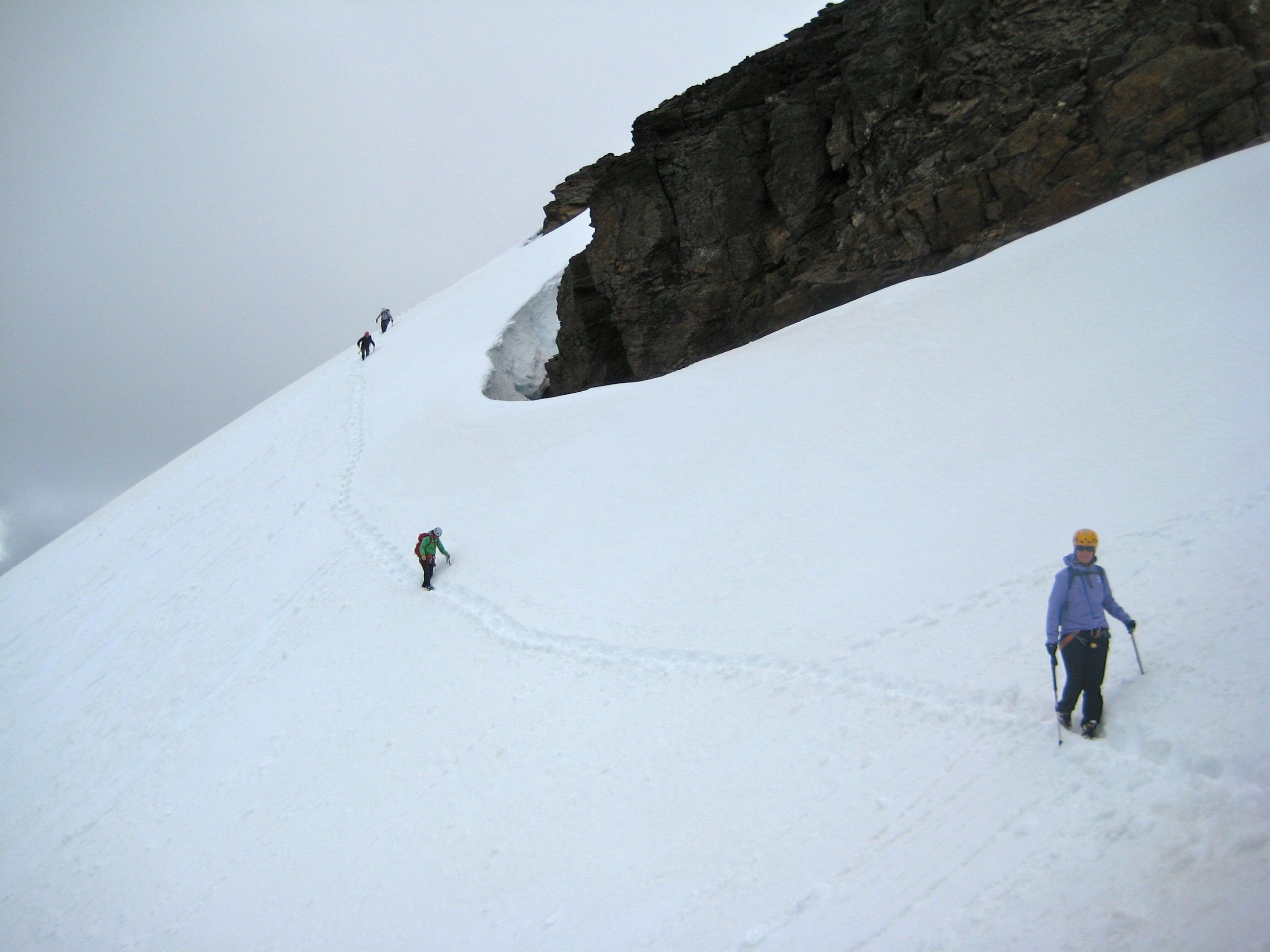 mountain climbers traversing steep snow slope below the rocky summit of Clark Mountain in the Glacier Peak Wilderness