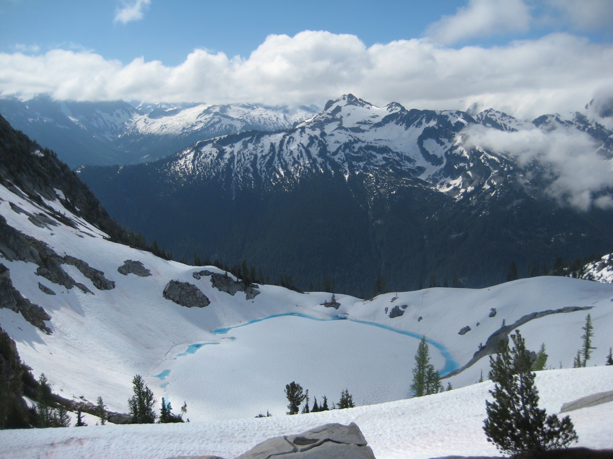 looking down on snow covered, slightly melted out Blue Lake and Saddle Bow Mountain from below Agnes Mountain in the Glacier Peak Wilderness