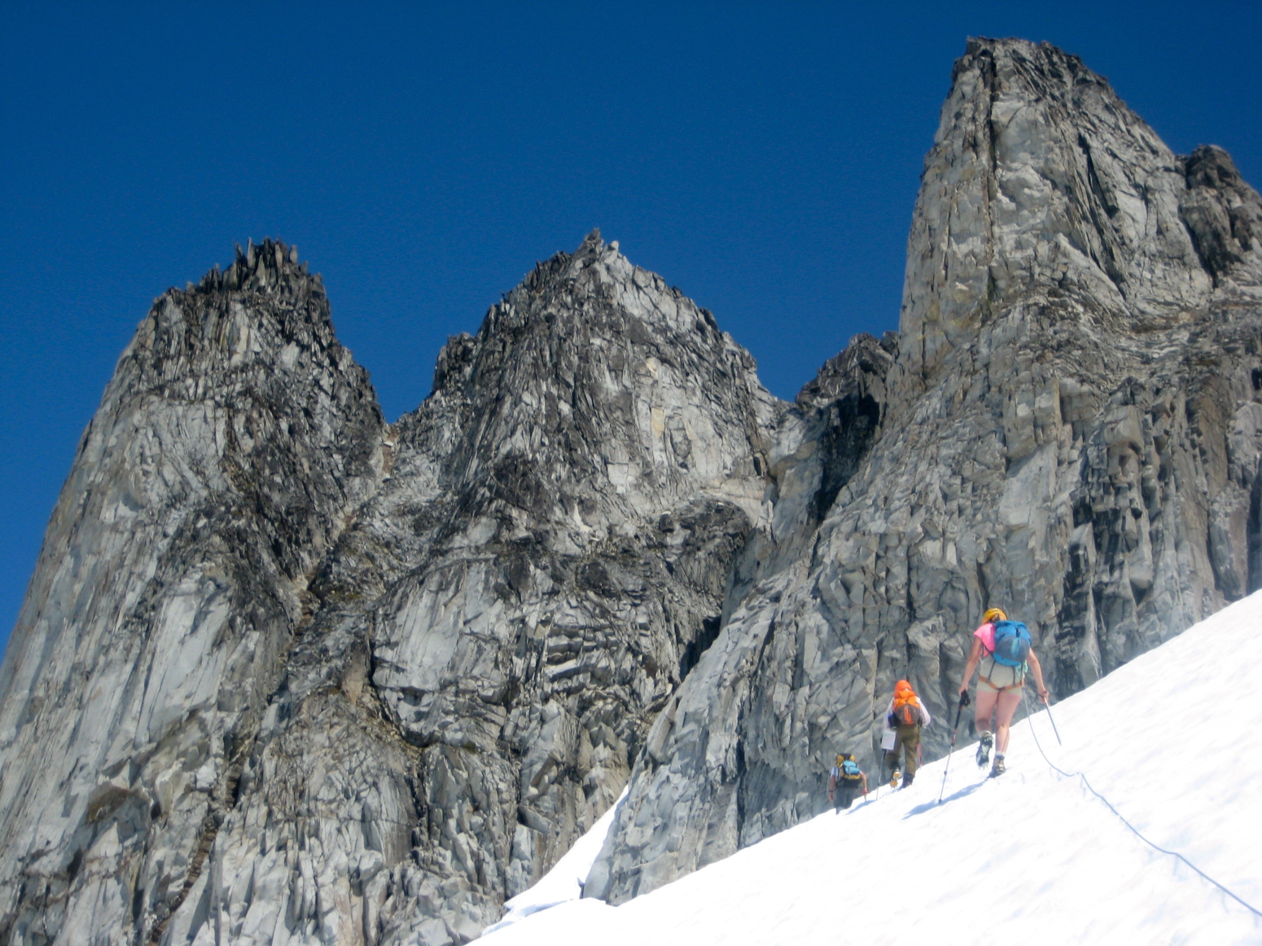 roped mountain climbers booting up the snow towards the rock, granite towers of Gunsight Peak in the Glacier Peak Wilderness