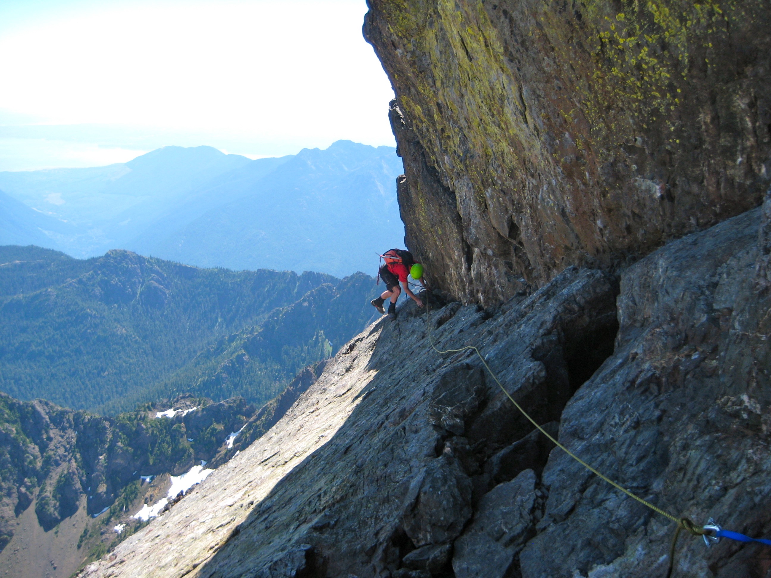 roped mountain climber scrambling the finger traverse on steep rock slabs on Mt Constance Outer Peak in the Olympic Mountains
