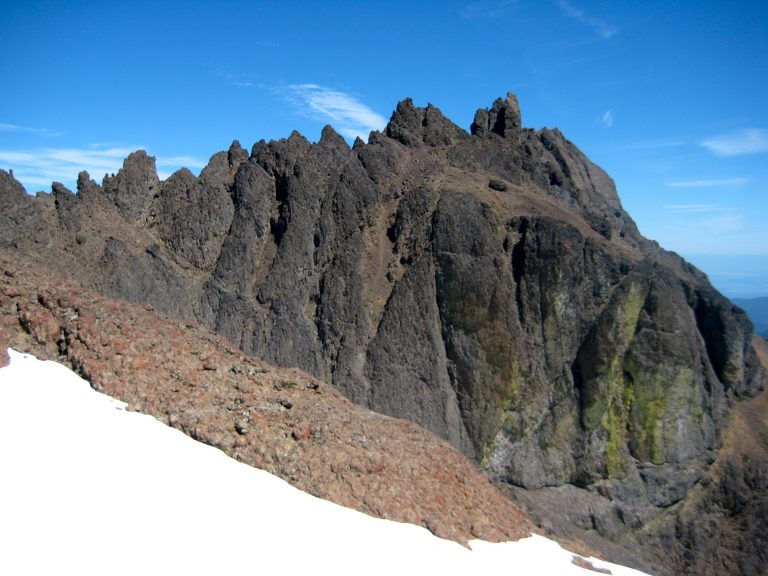 Craggy black summit ridge of Mt Constance Outer Peak contacts a blue sky in the Olympic Mountains