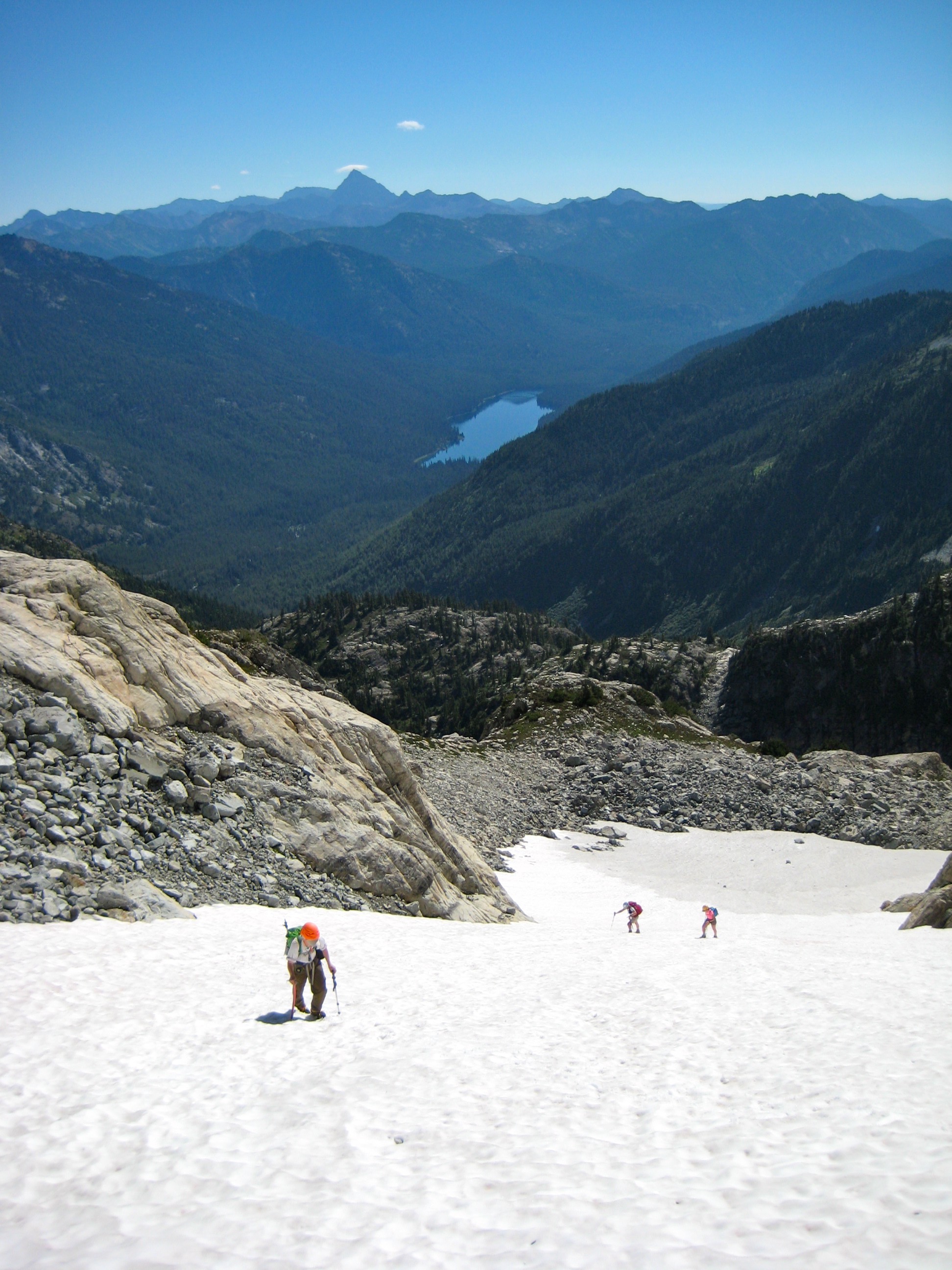 mountain climbers booting up snow couloir on Summit Chief Mountain surrounded by scree with alpine lakes in the background