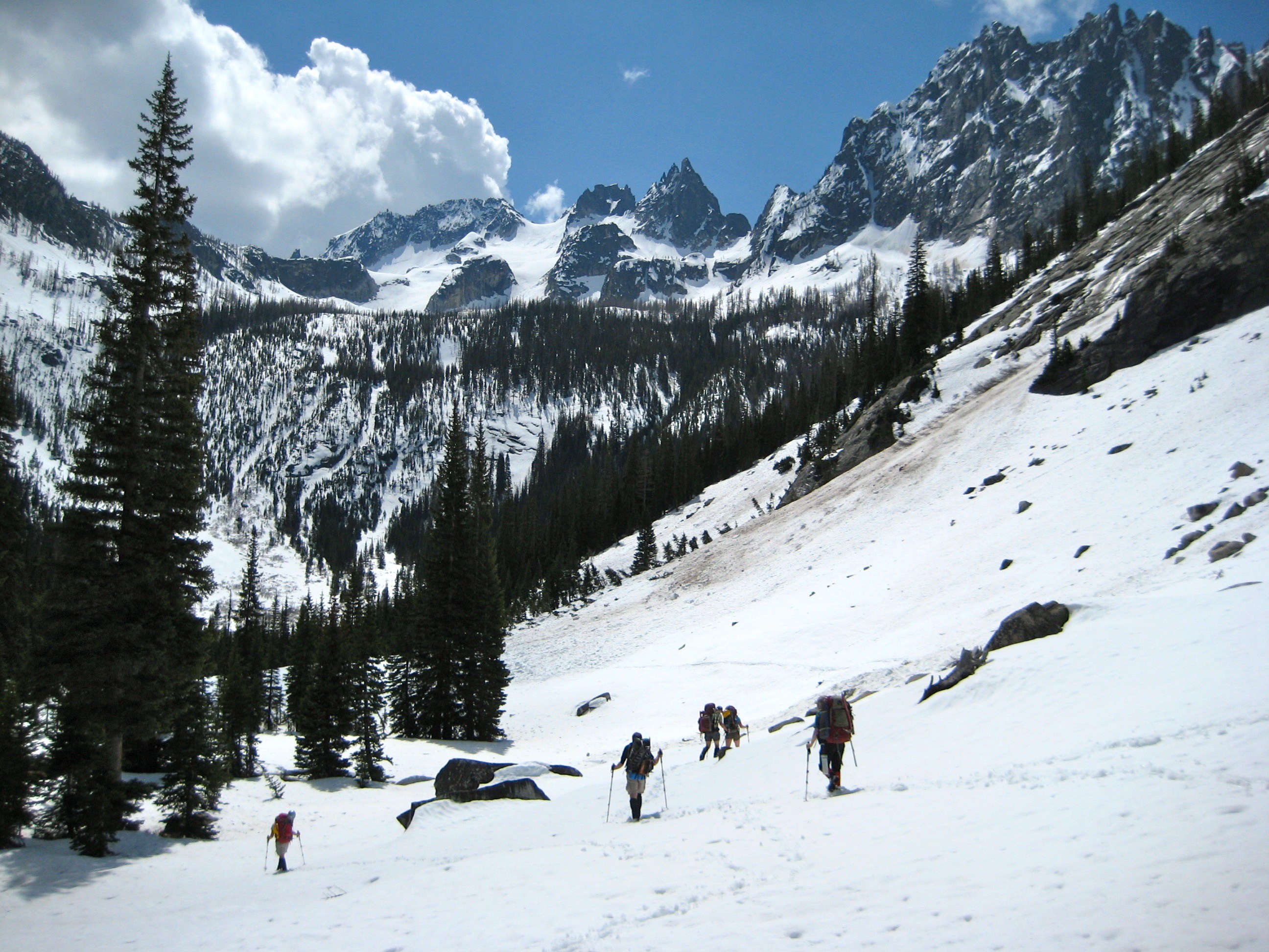 mountain climbers descending snow covered basin with random evergreen tree with Silver Star Mountain and the Wine Spires in the Mazama Mountains filling the sky line