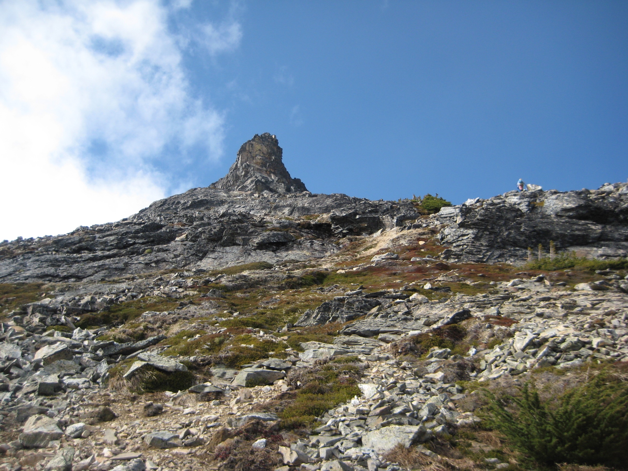 Looking up broken rock and scree toward the summit horn of Paul Bunyans Stump in the McAllister Mountains in North Cascades National Park