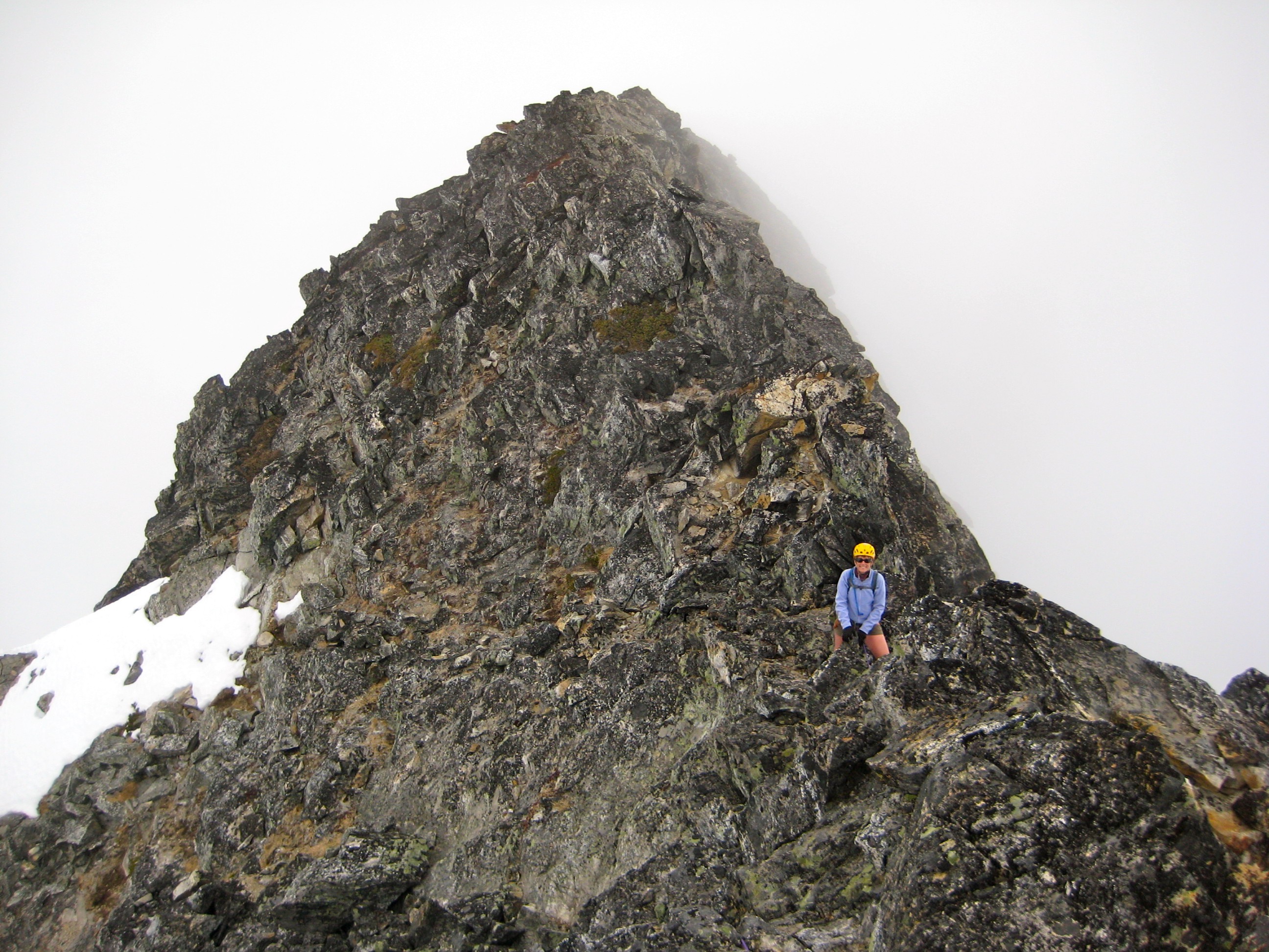 mountain climber belaying on the rocky ridge of Paul Bunyan's Stump in the McAllister Mountains with linguring snow patch