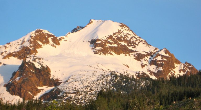 Evening sun warms the red rock and large snowfield of North Twin Sister