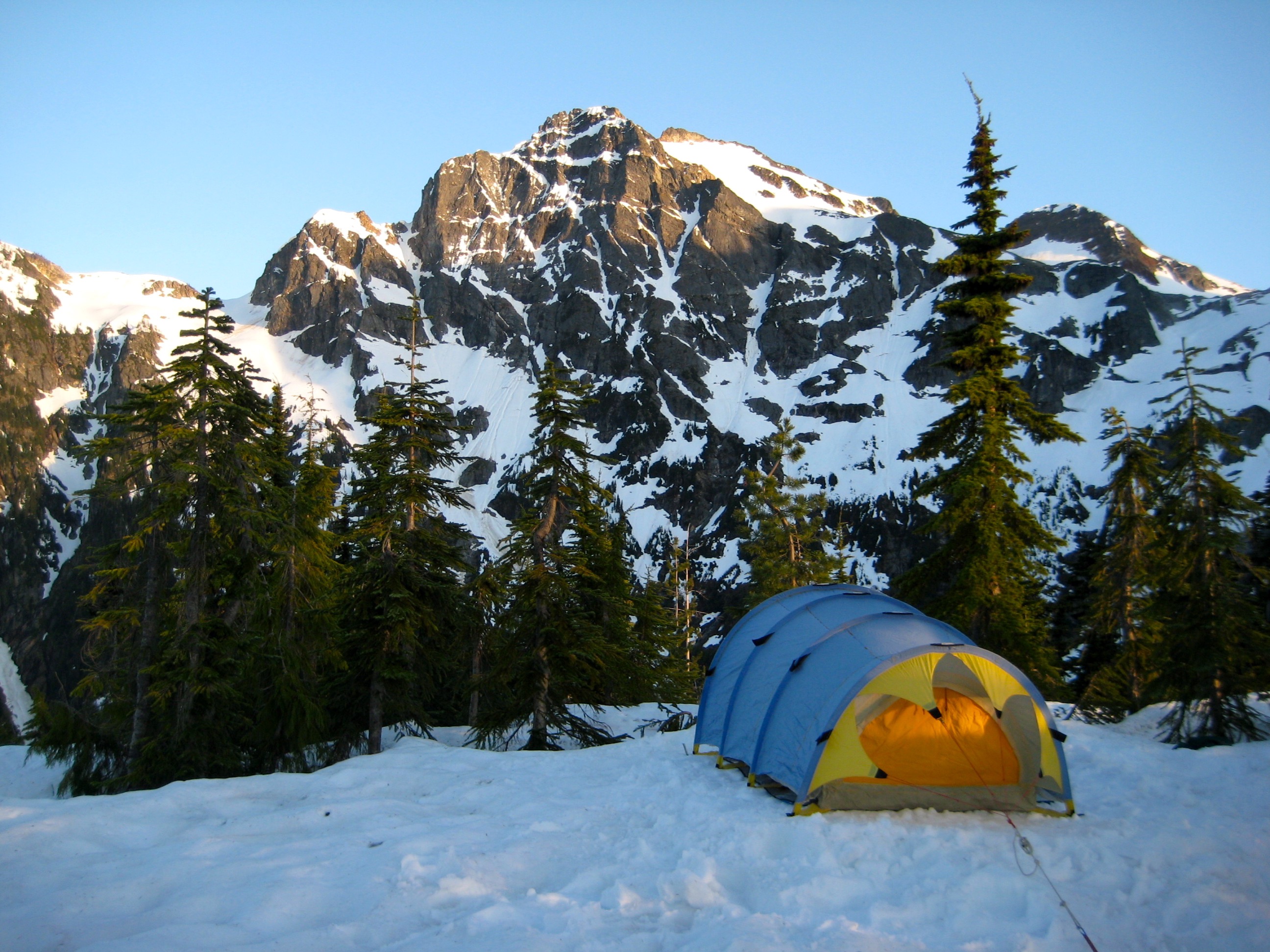 evening light on Colonial Peak in the McAllister Mountains with linguring snow fields with a mountain climber's tent in the foreground pitched on a snow covered knob in North Cascades National Park