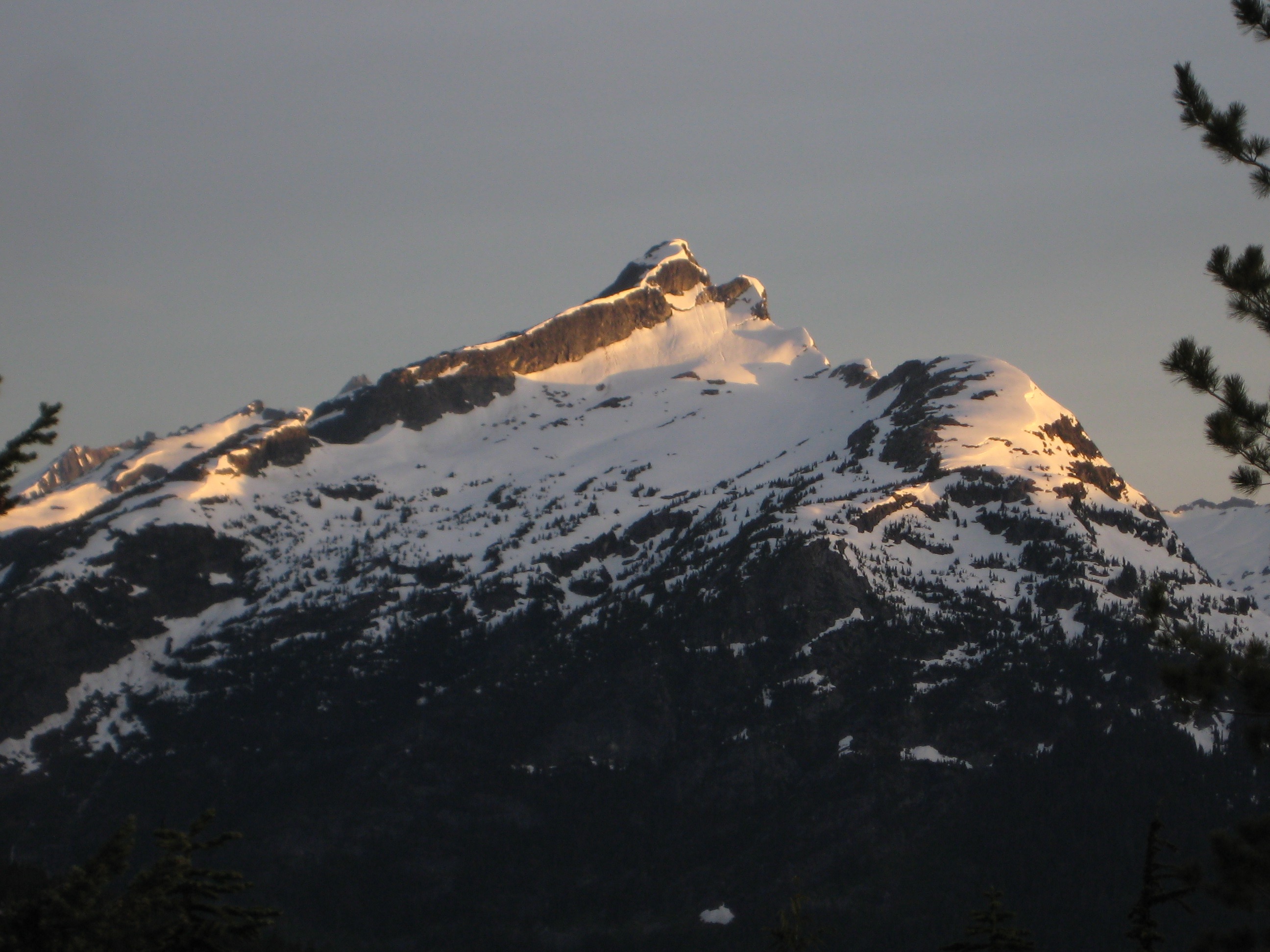 morning sun lighting up the summit horn of David Peak in North Cascades National Park with large snow fields
