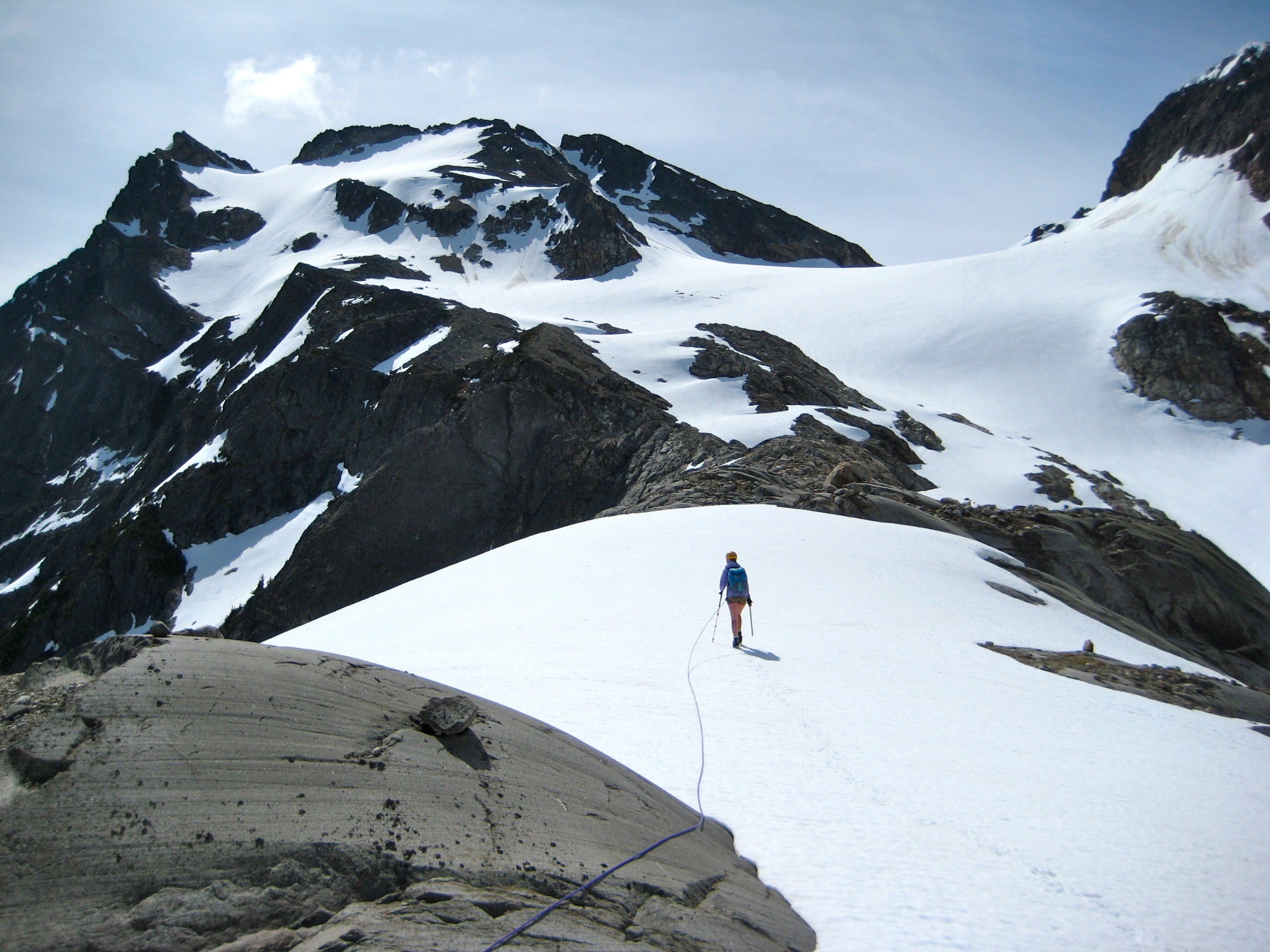 roped mountain climber boots up large snow field toward Colonial Peak in the McAllister Mountains which fills the sky line