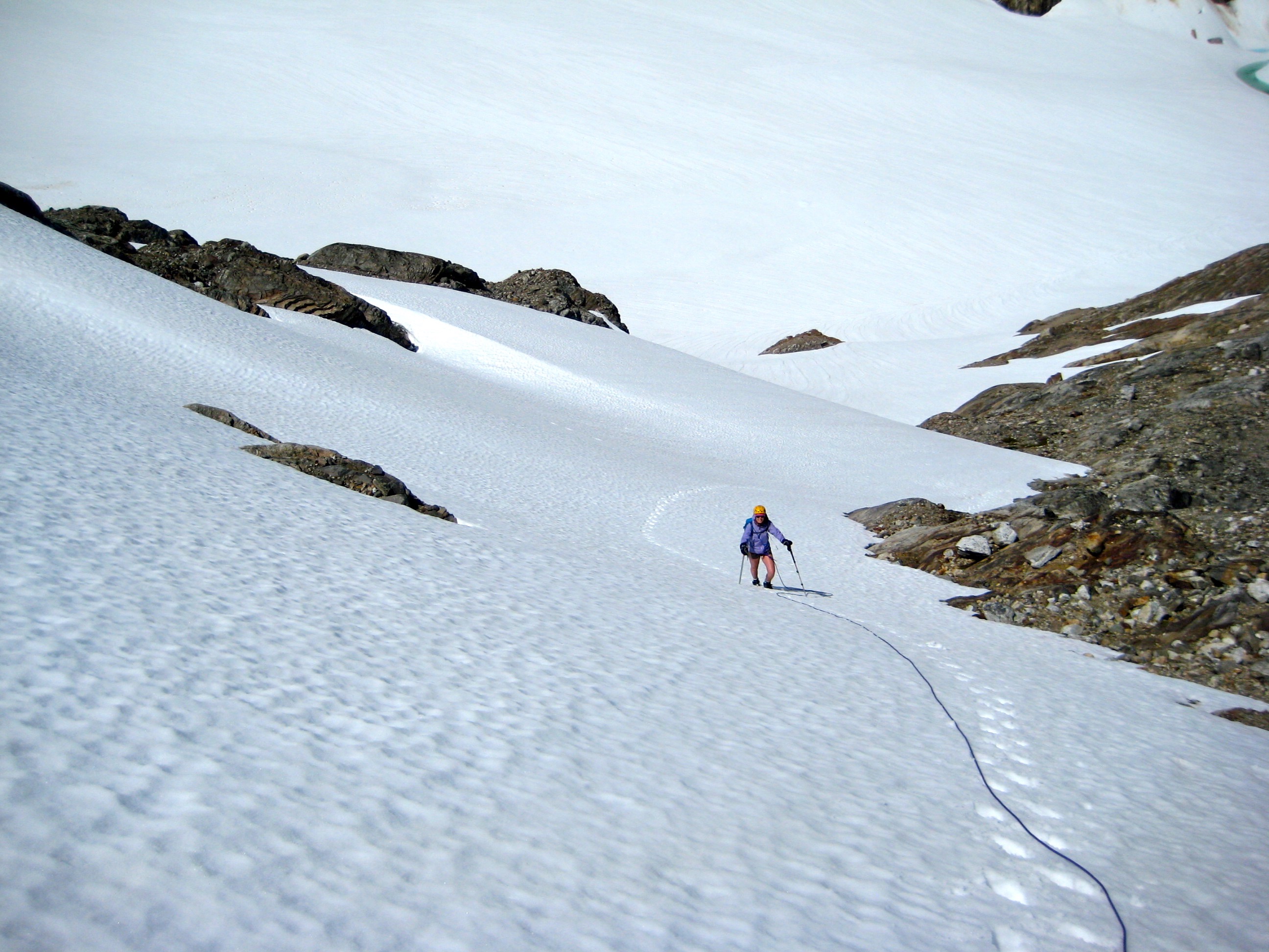 looking down on roped mountain climber booting up steep snow slope above the Colonial Glacier in the McAllister Mountains