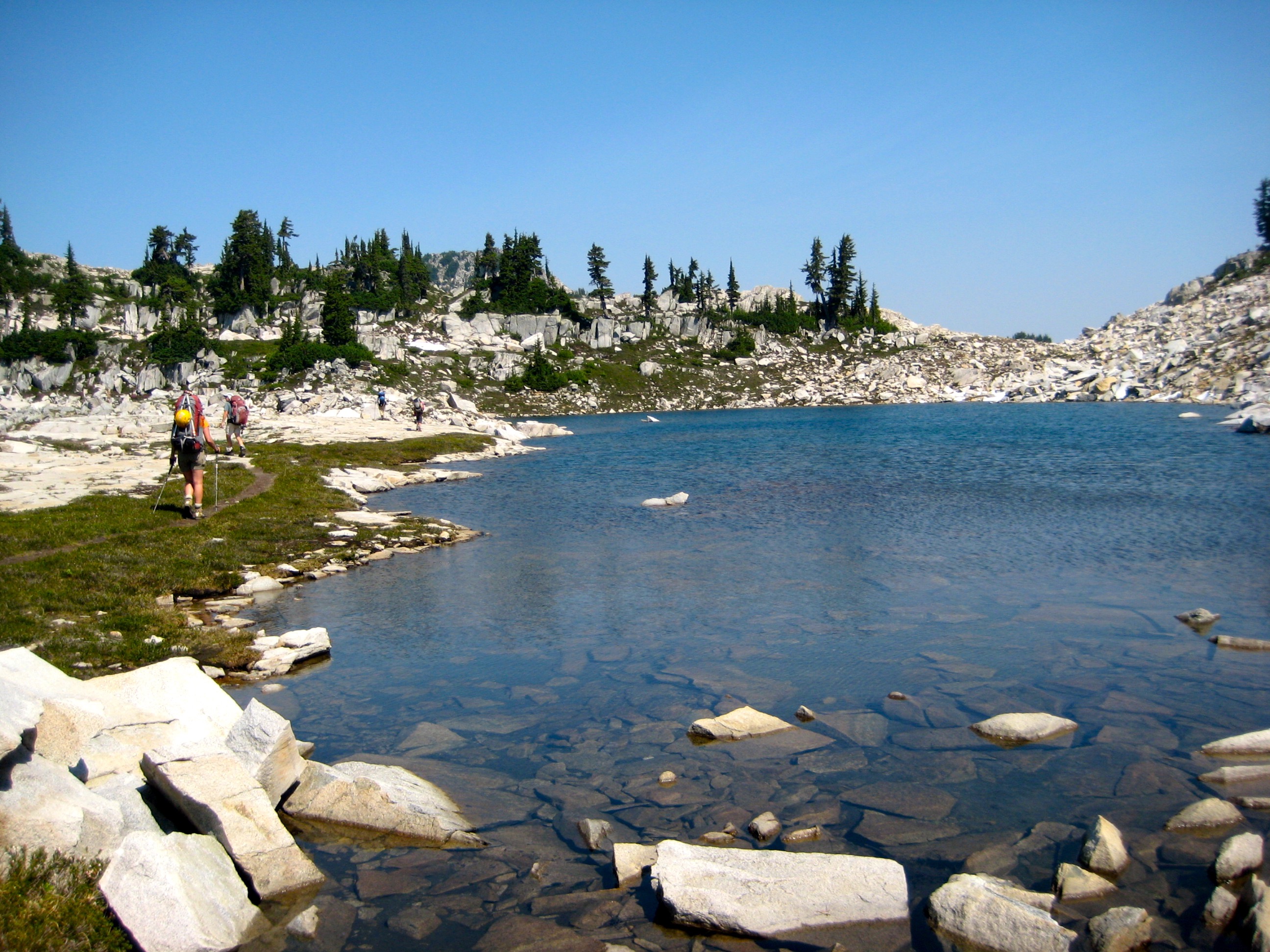 backpackers hiking around Upper Tank Lakes in the Alpine Lakes Wilderness with heather and granite boulder shoreline
