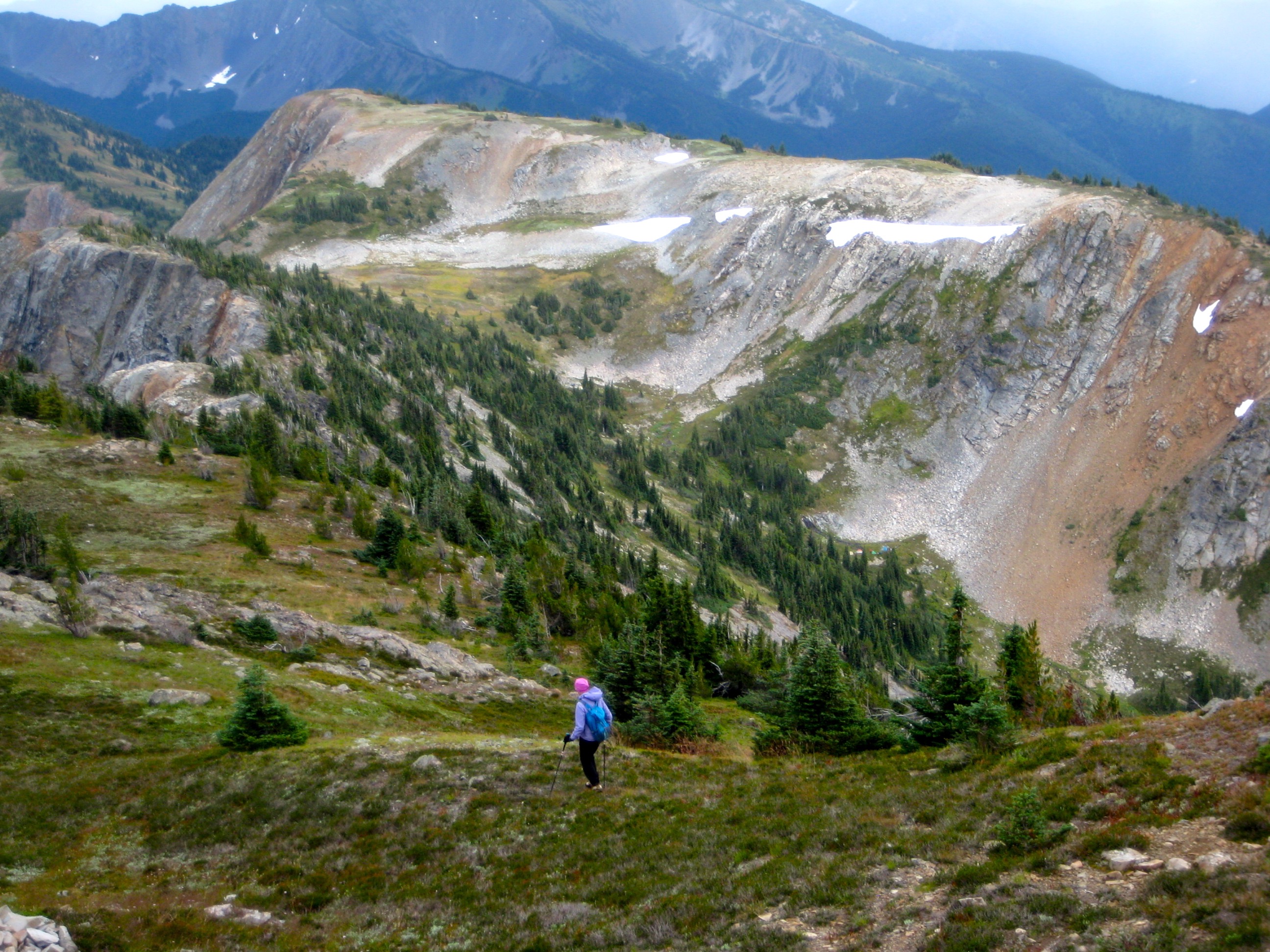 hiker descending grass slope with Devils Dome on the Jack Mountain circuit in the Upper Skagit Mountains in the distance