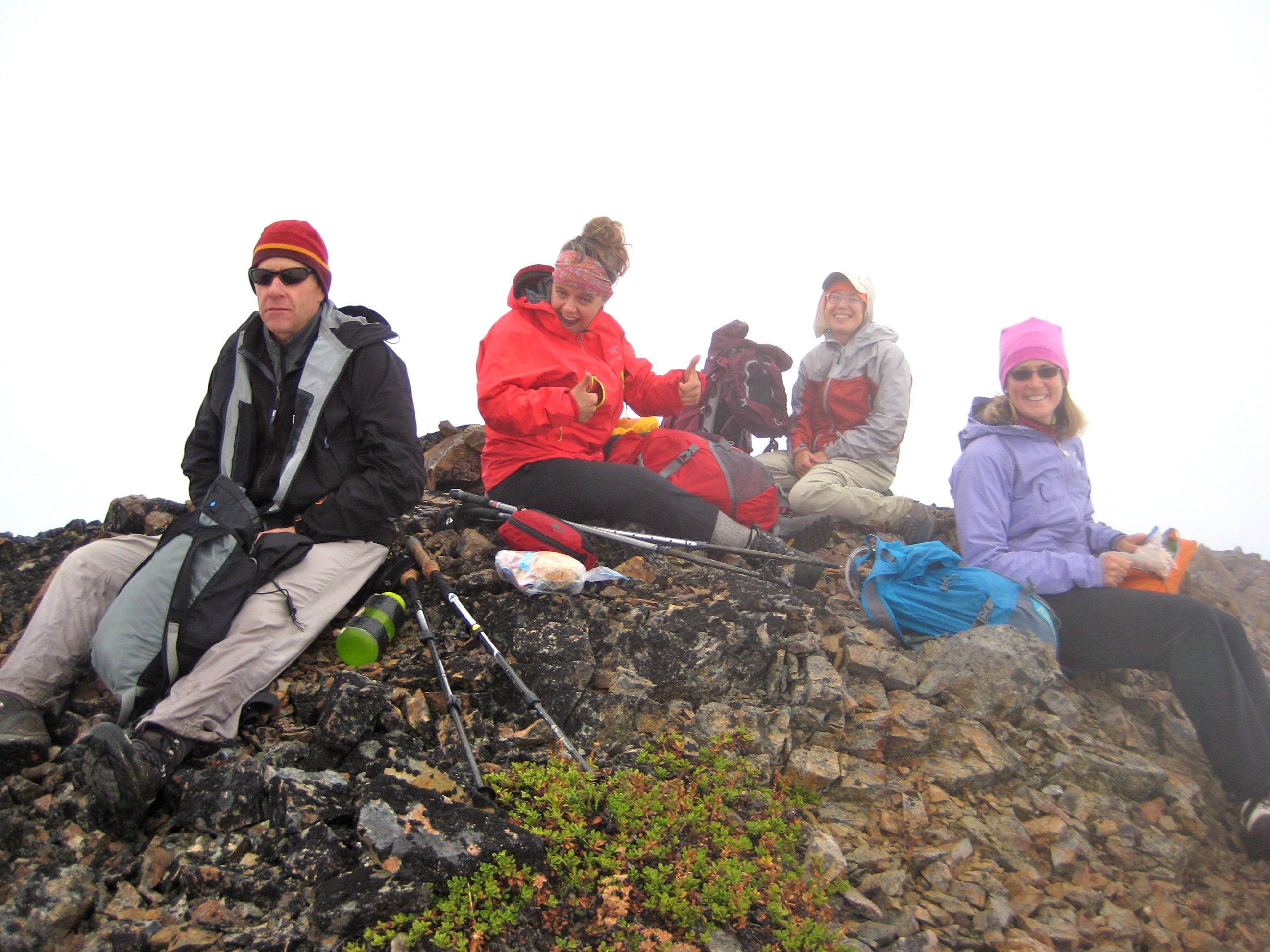 hikers taking a break on the rock summit of Daemon Peak in the Upper Skagit Mountains