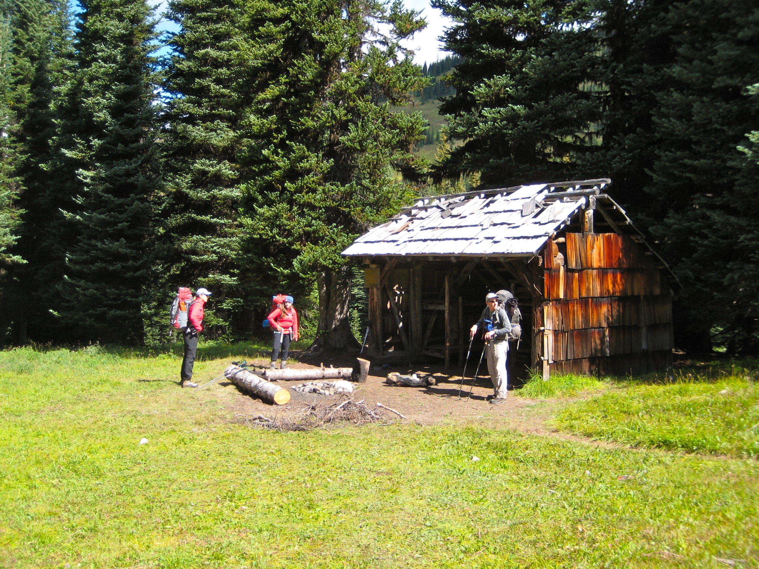 backpackers standing at Devils Park shelter in the Upper Skagit Mountains on the Jack Mountains Circuit Trail with meadow grasses and evergreen trees