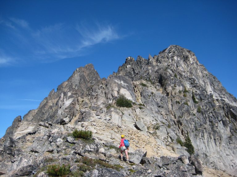A mountain climber scrambles up a steep gray face on Azurite Peak