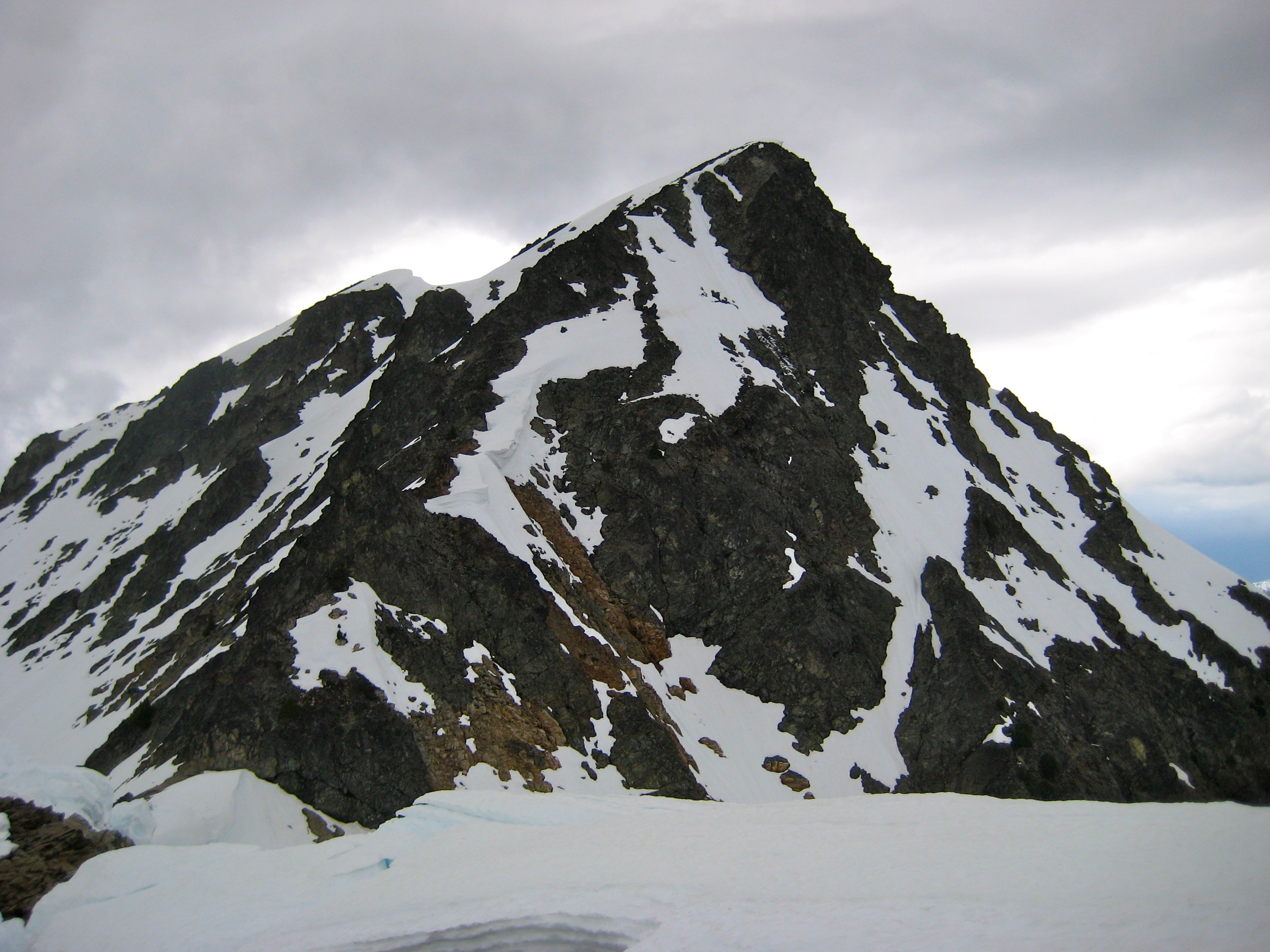 The pyramidal summit of Kitling Peak rises above a snowy ridge