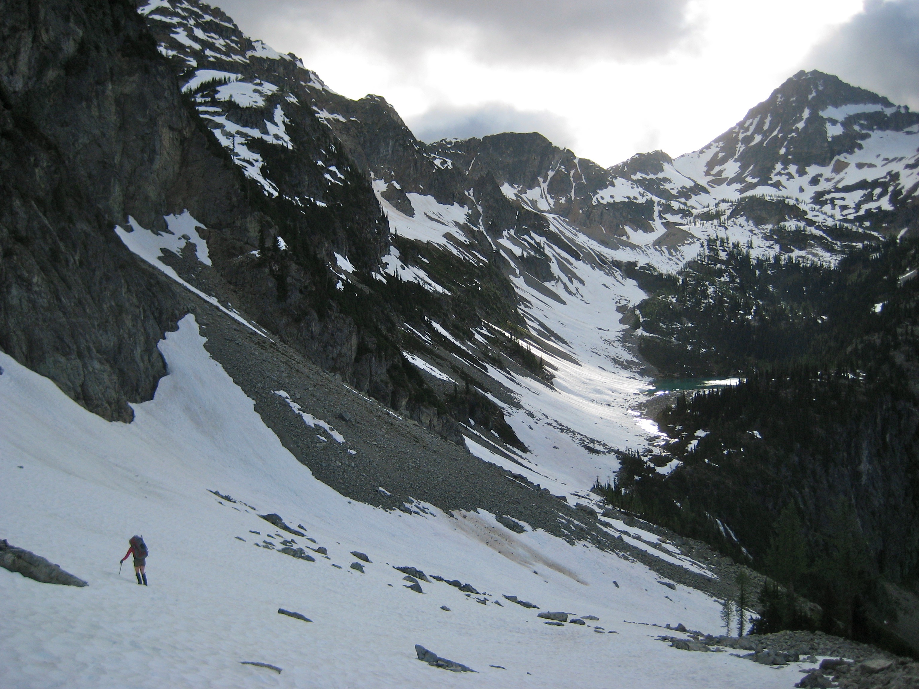 mountain climber descending snow field with Black Peak in the Ragged Ridge Mountains in North Cascades National Park