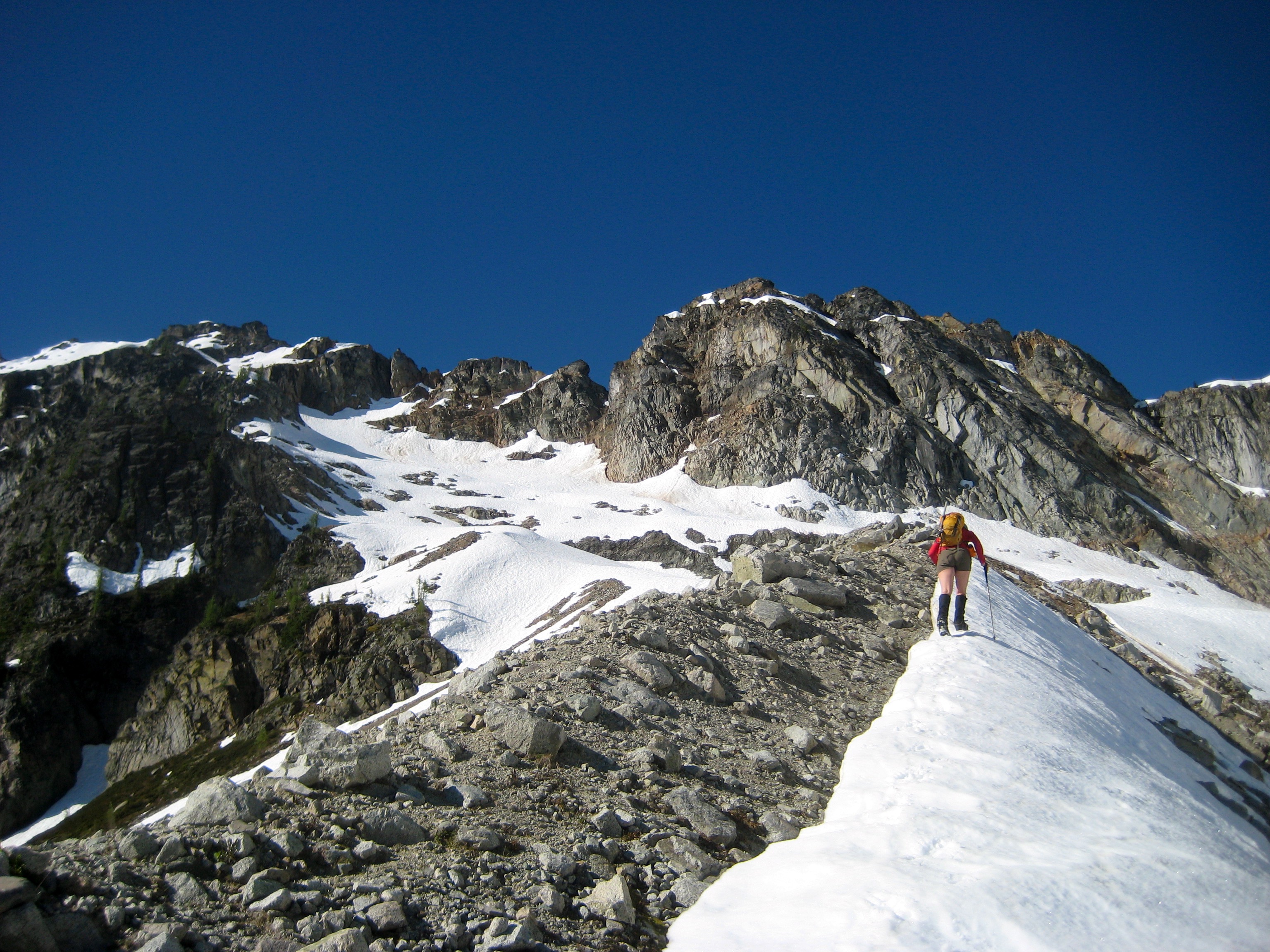 mountain climber ascending linguring snow on the Lewis Glacier Moraine with Corteo Peak in the Ragged Ridge Mountains in North Cascades National Park