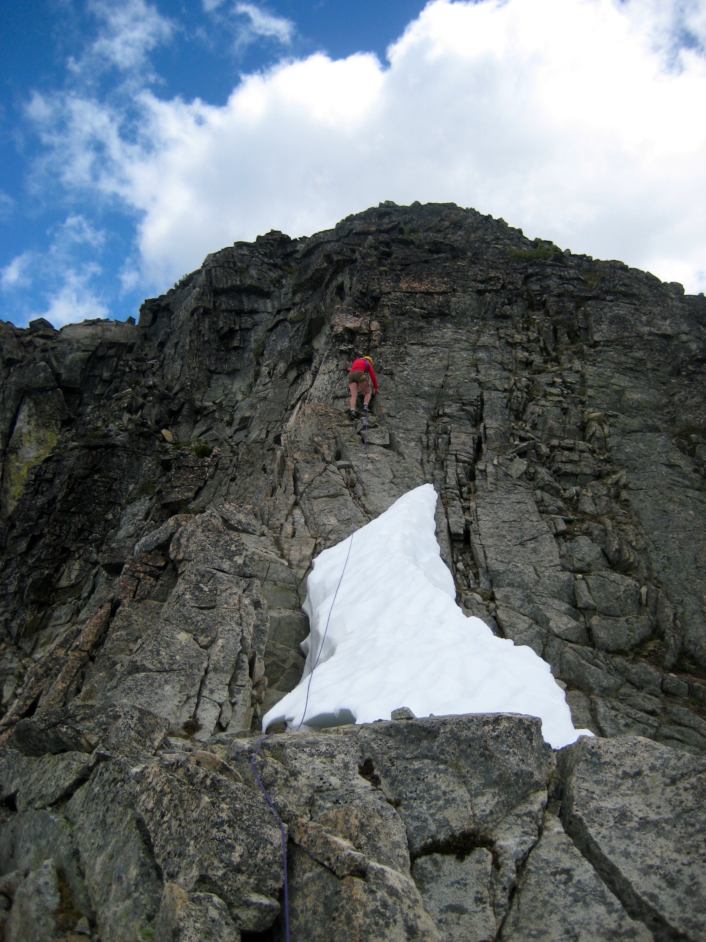 lead, roped mountain climber on rocky, ridge with linguring snow patch on the SW Ridge of Corteo Peak in the Ragged Ridge Mountains in North Cascades National Park