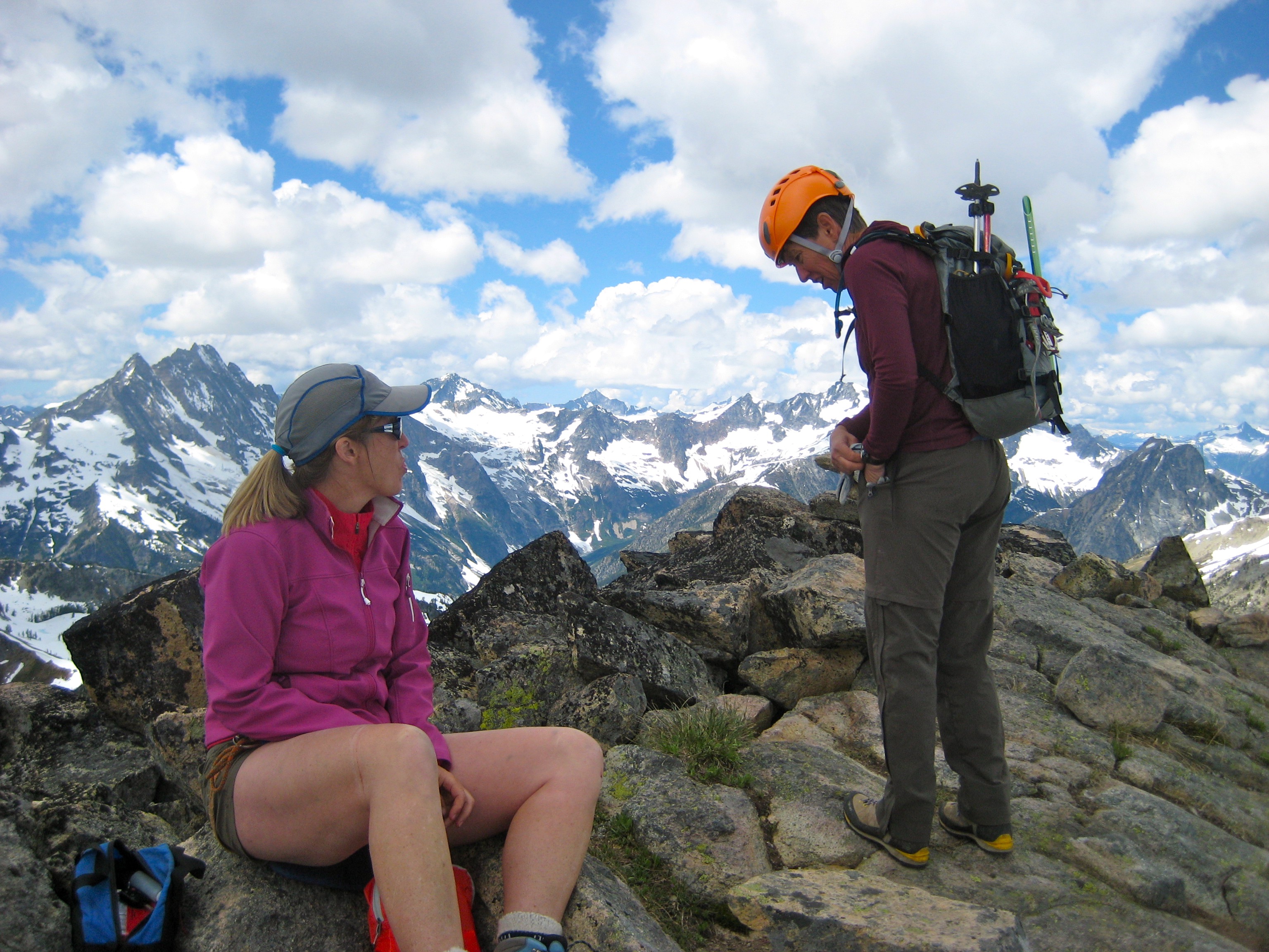 mountain climbers taking a break on the rocky summit of Corteo Peak in the Ragged Ridge Mountains with the North Cascade Mountains in the background