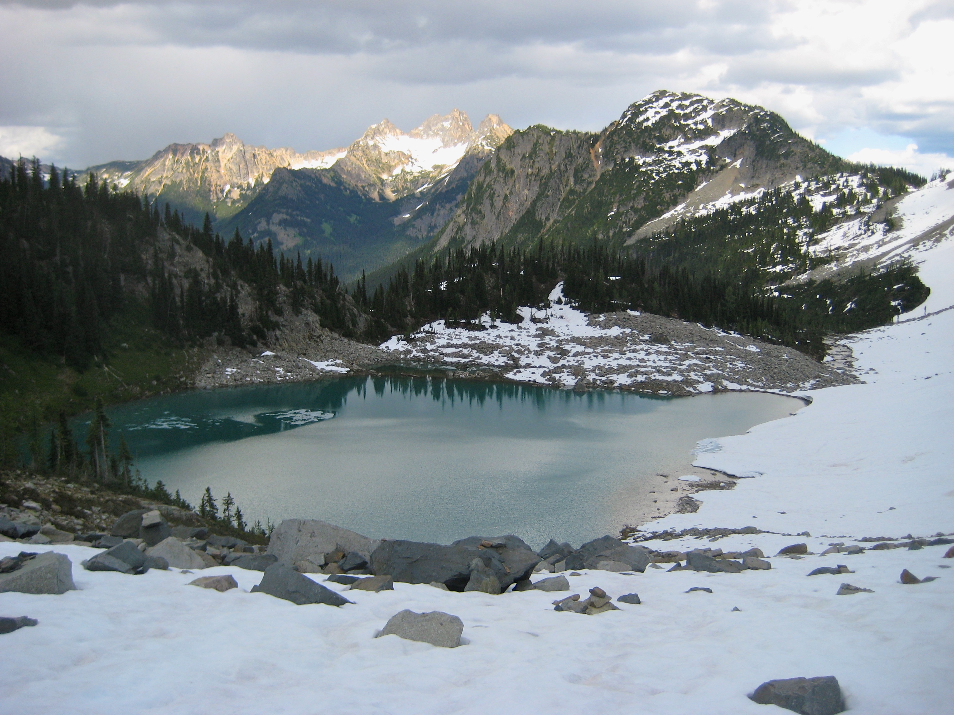 Cutthroat Peak above Lewis Lake with snow on the shoreline in the Ragged Ridge Mountains in North Cascades National Park