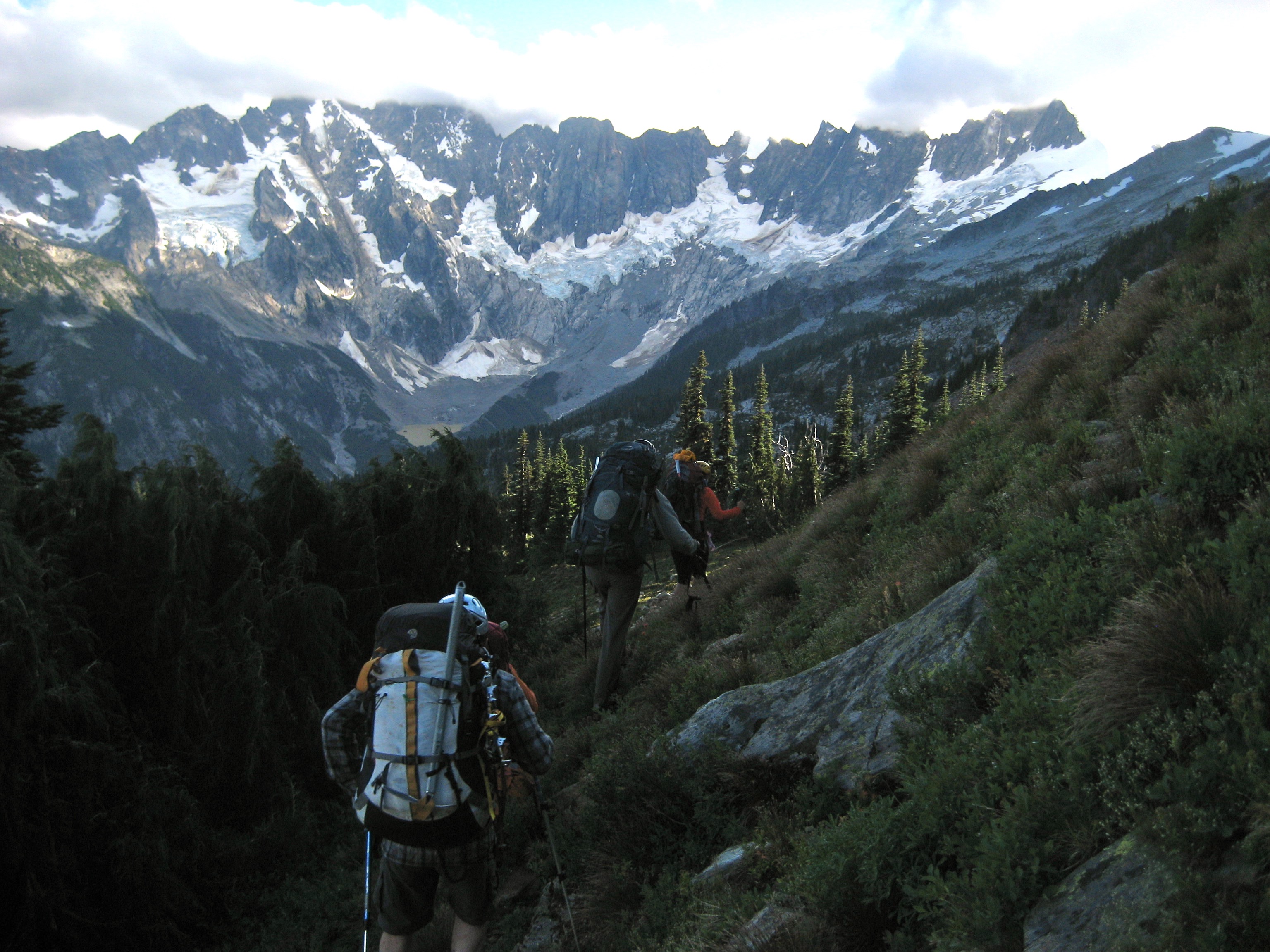 climbers traverse alpine slopes with grass and small trees heading towards Northern Picket mountain range