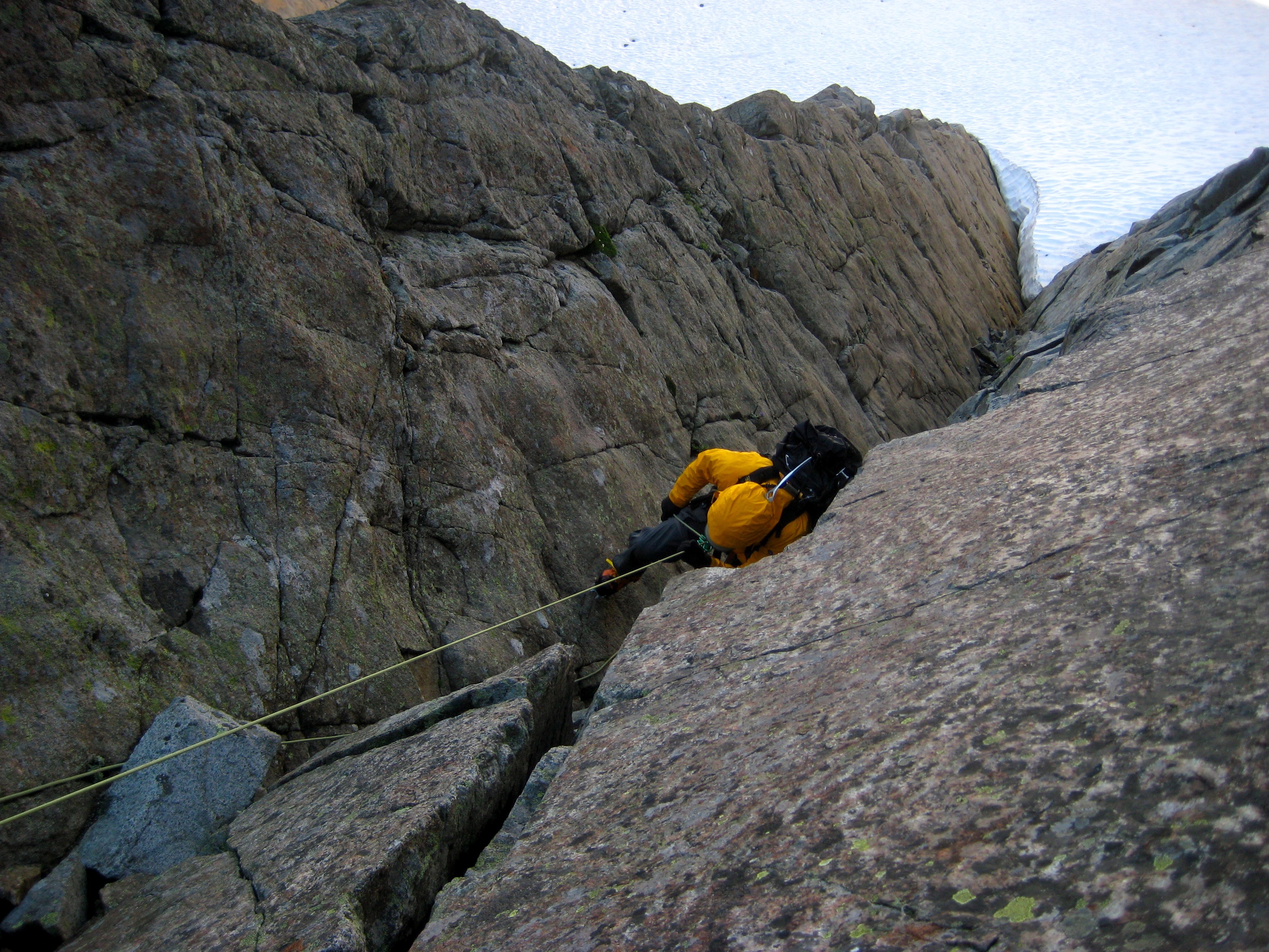 climber rappelling down rock slab to snow field