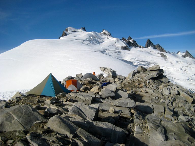 mountain climbers tents sit on rocky Challenger Arm moraine below the large Challenger Glacier and the summit of Mt Challenger in the Northern Picket Range