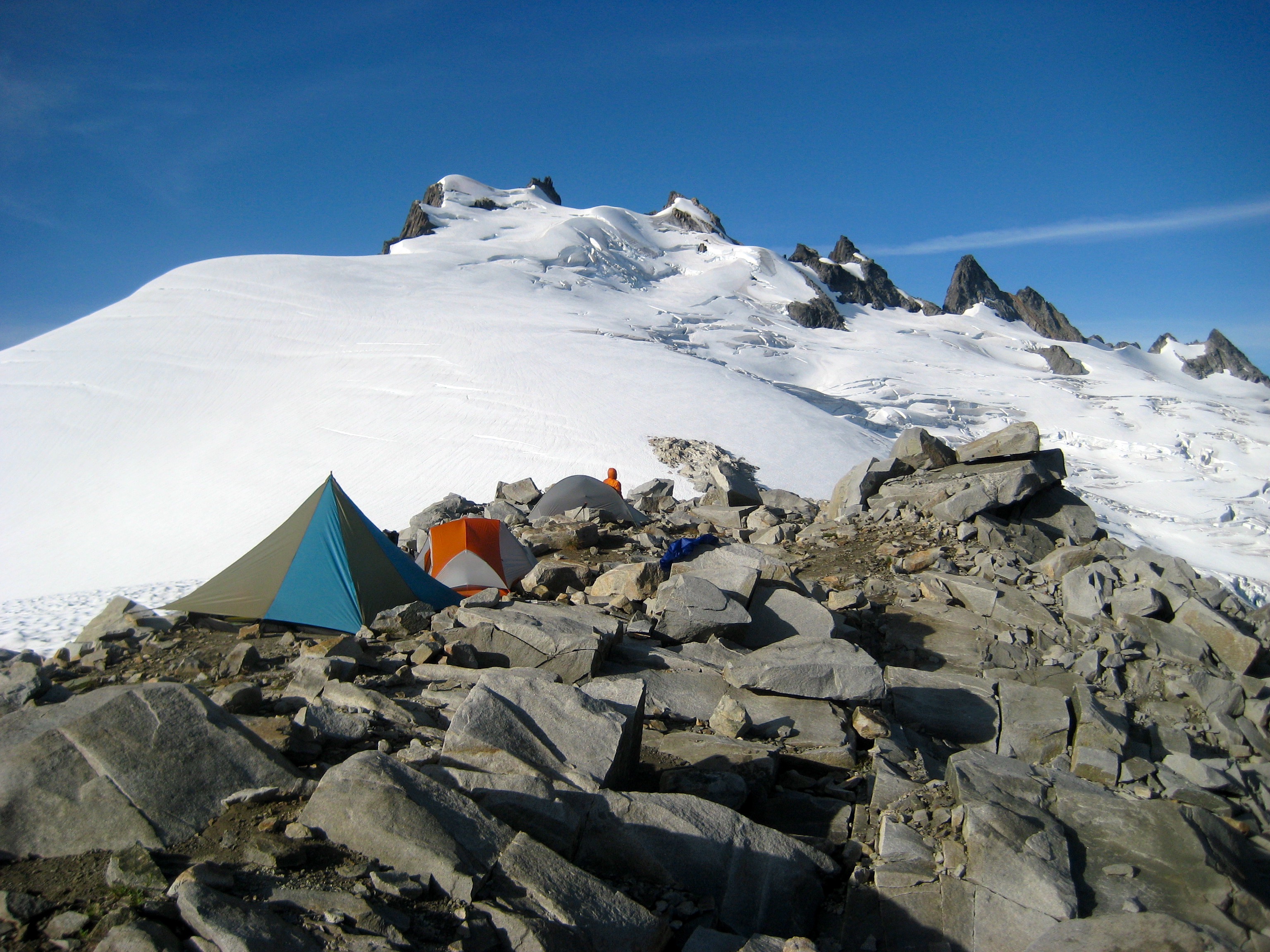 mountain climbers tents sit on rocky Challenger Arm moraine below the large Challenger Glacier and the summit of Mt Challenger in the Northern Picket Range