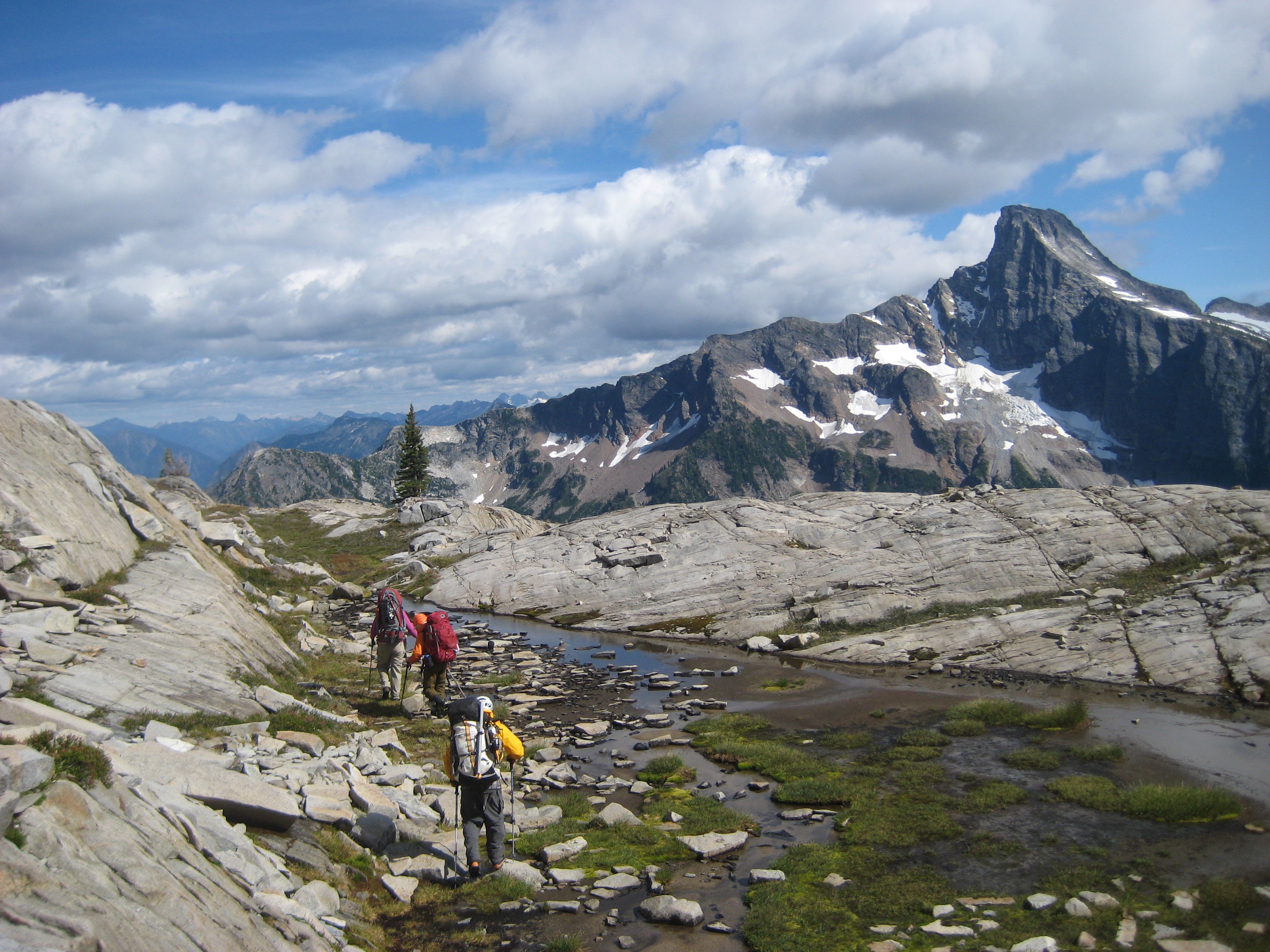 climbers hiking along Wiley Ridge with lingering snow patches and exposed rock slabs