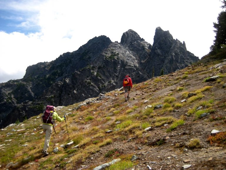 Hikers ascend a grassy slope toward the triple-peaked Three Queens Mountain